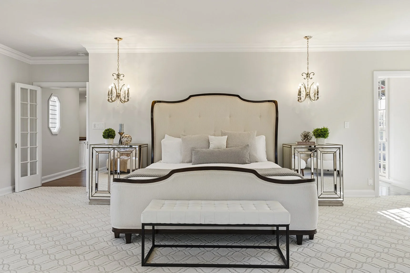 Elegant neutral-toned bedroom with upholstered bed, mirrored nightstands, crystal chandeliers, and bench