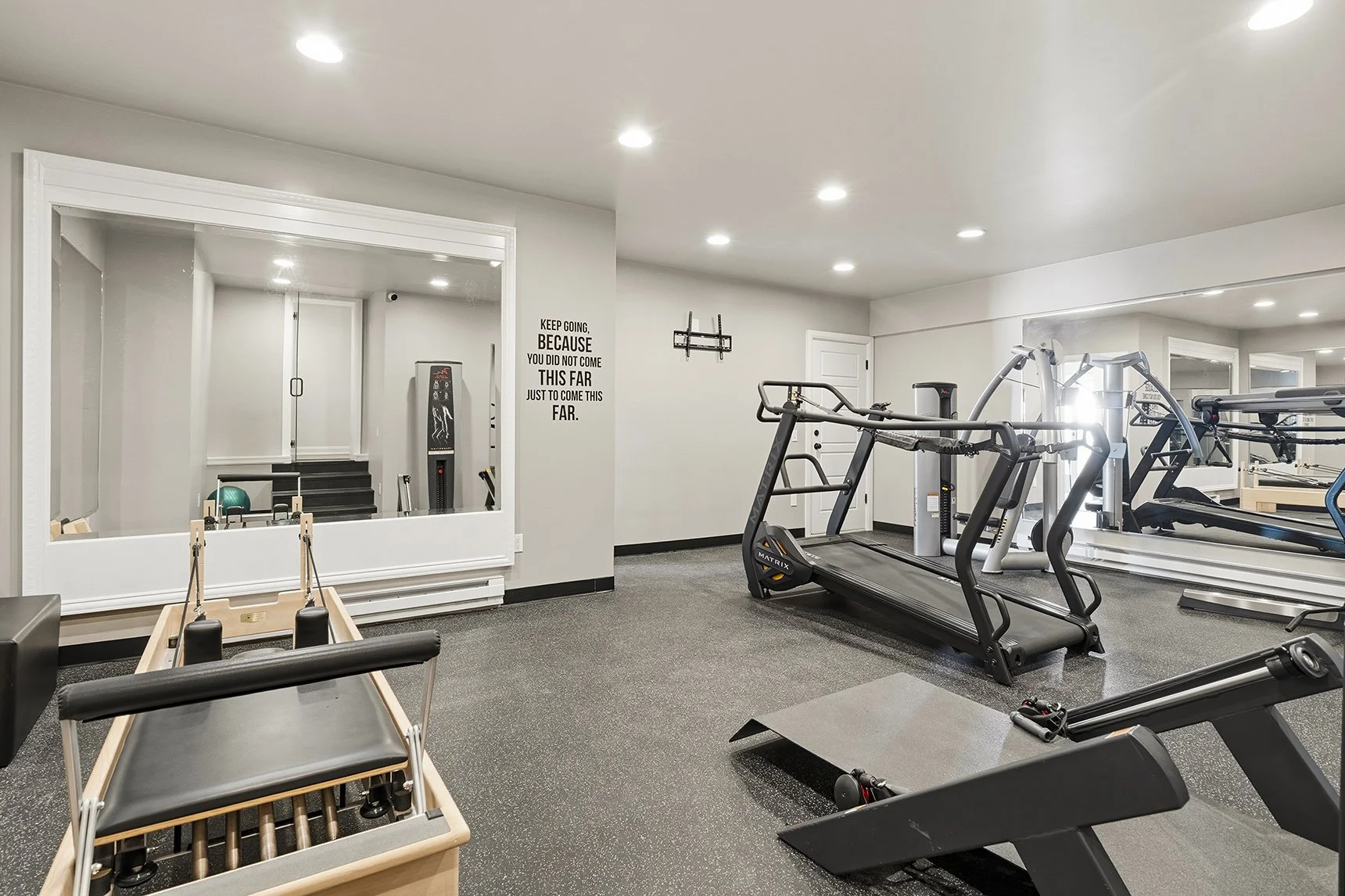 Bright modern fitness room with treadmills, Pilates reformer, strength equipment, wall mirrors, and motivational quote