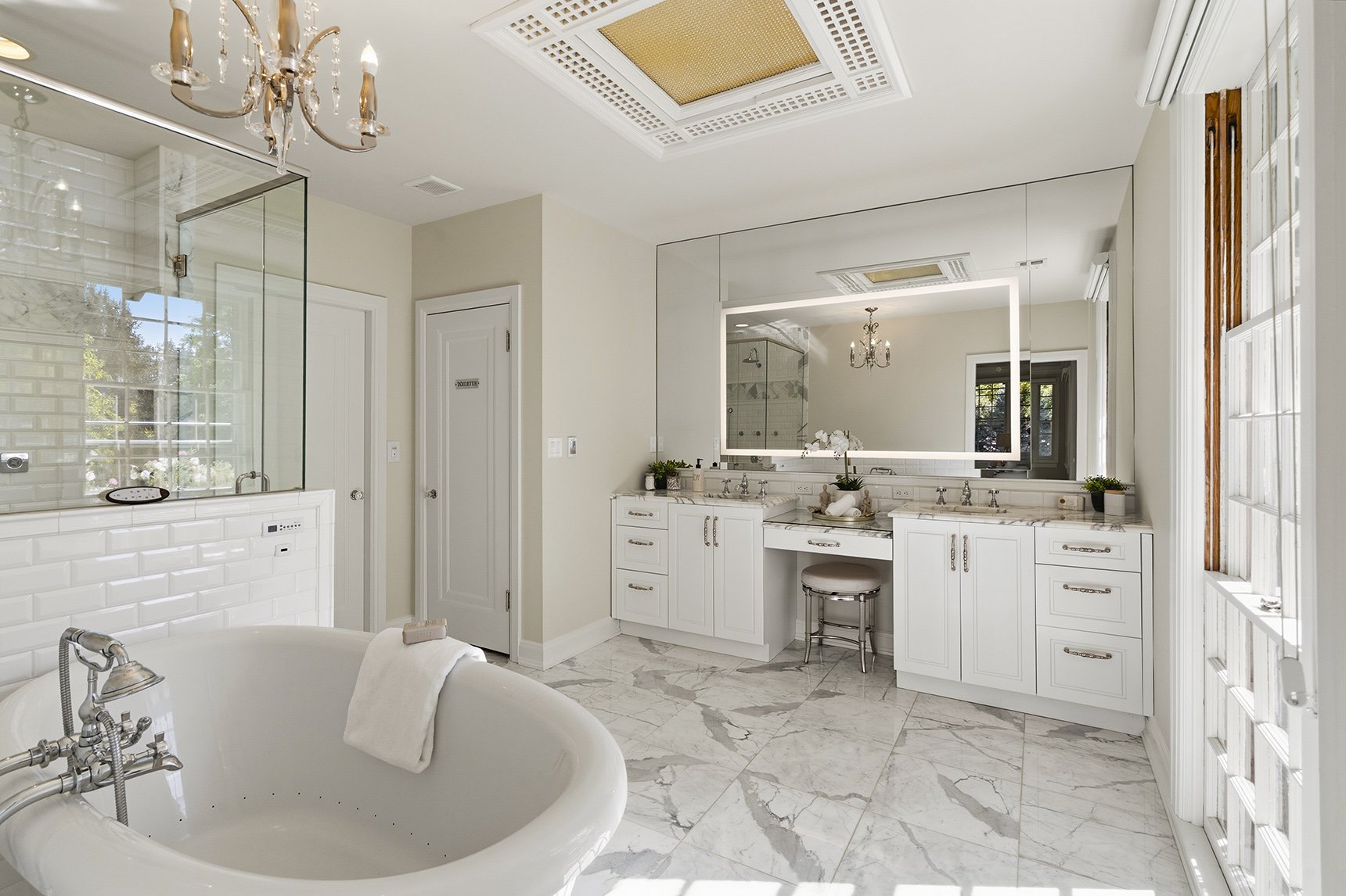 Luxurious bathroom with a white clawfoot bathtub, marble floors, a large mirror, double vanity with marble countertops, and a glass-enclosed shower.
