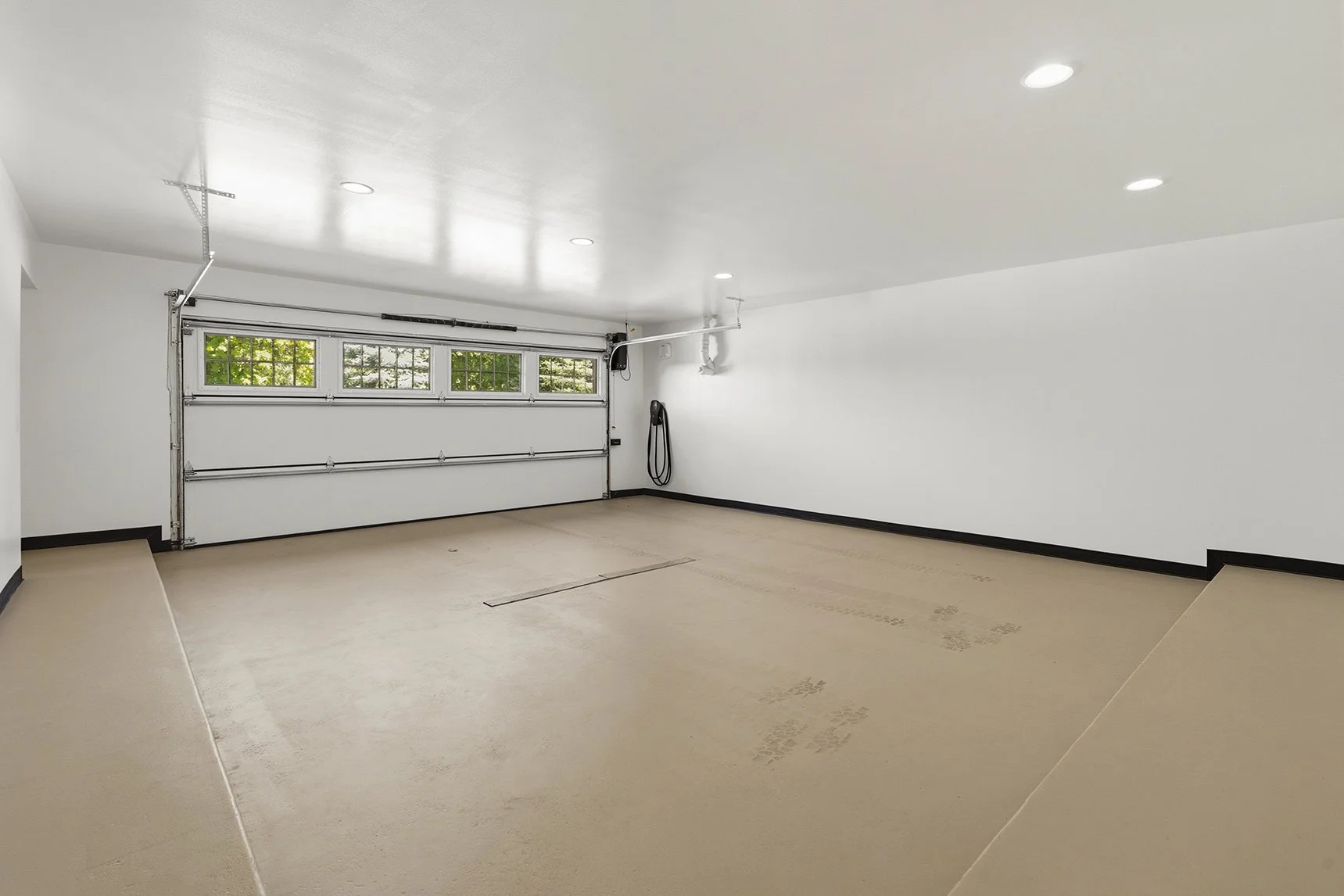Clean, spacious residential garage with a white sectional door, windows, recessed lighting, and a wall-mounted hose.
