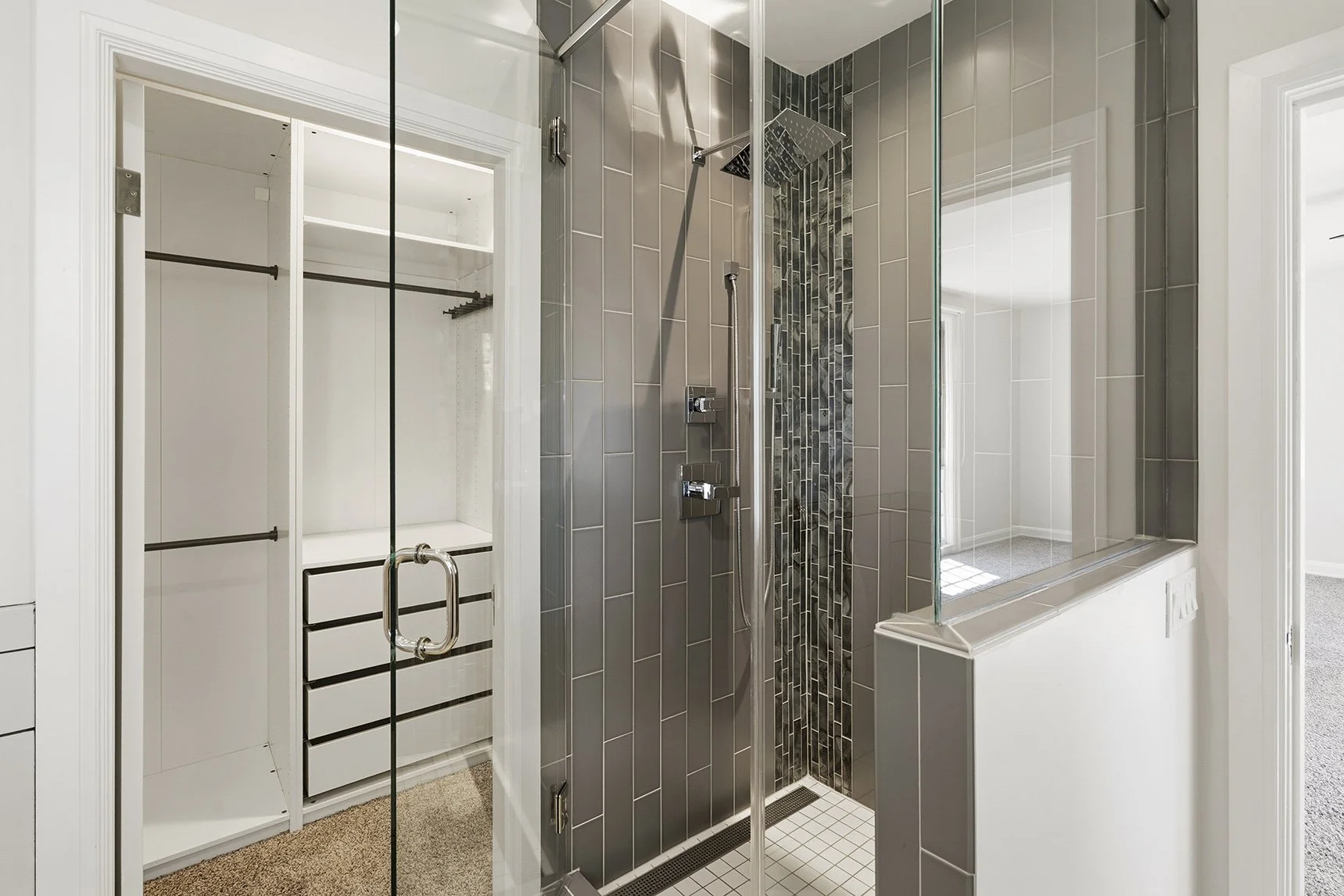 Modern bathroom with a glass-enclosed walk-in shower, gray tile walls, handheld showerhead, and adjacent white built-in closet