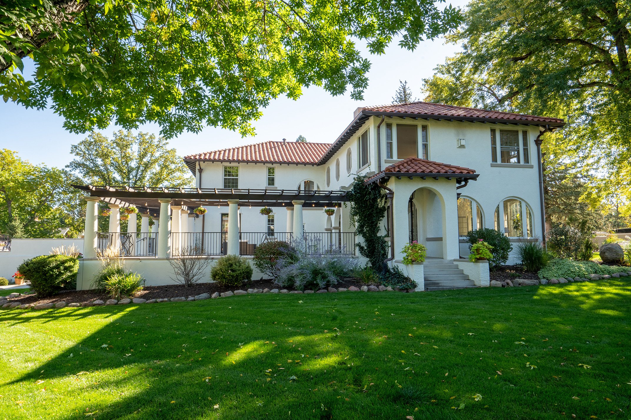 Mediterranean-style stucco house with red tile roof, covered patio, landscaped garden, and green lawn