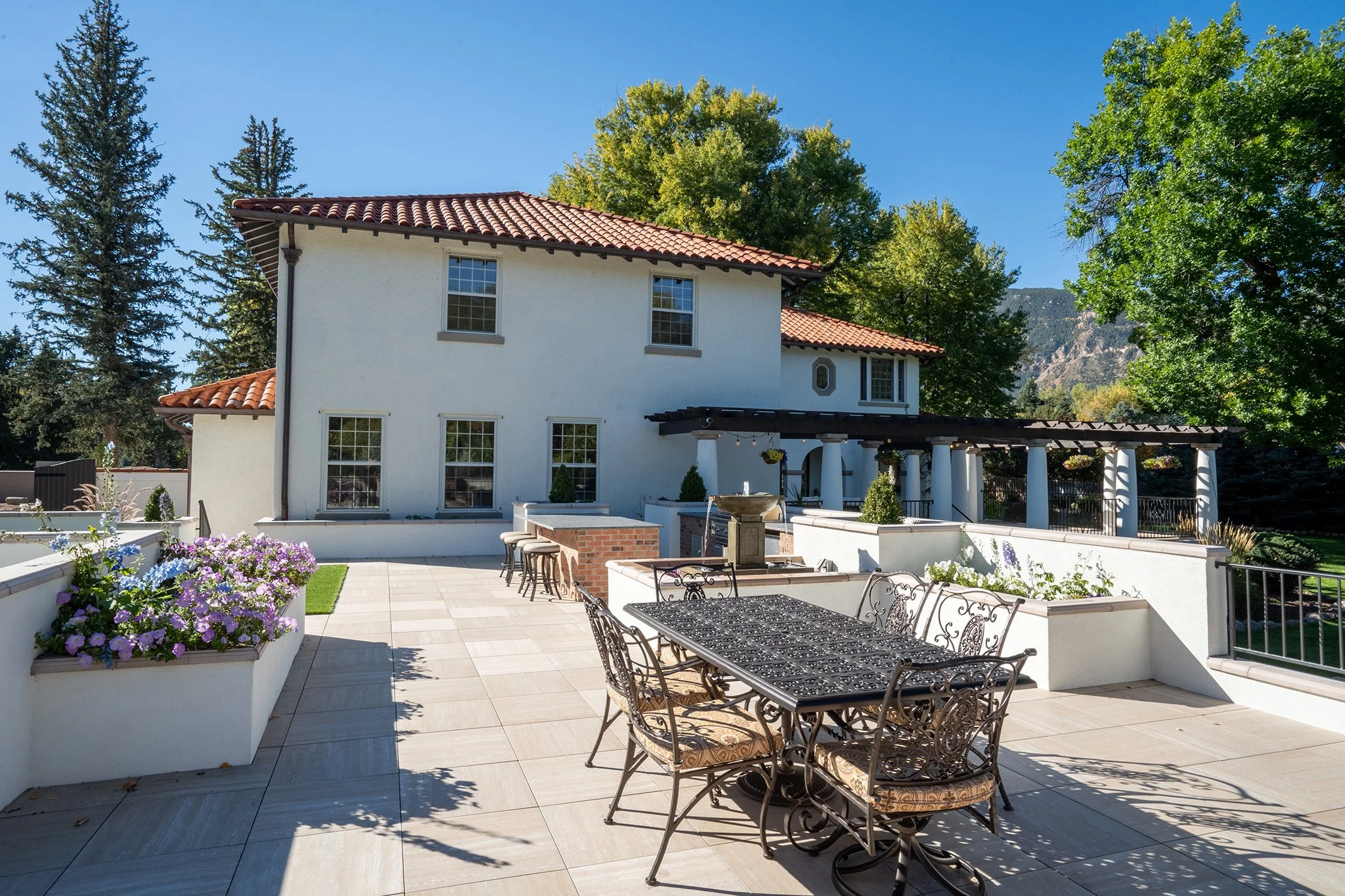 Spanish-style home with terracotta tile roof, landscaped patio, fountain, outdoor dining table, and mountain views