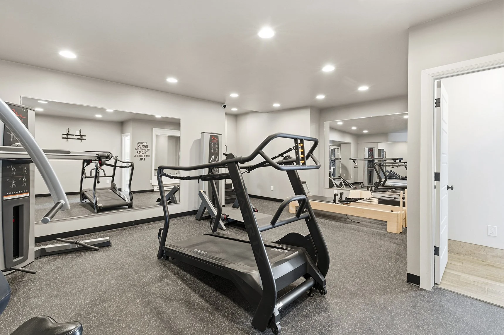 Empty home gym with treadmills and weight equipment, white walls, ceiling lights, and a large mirror.