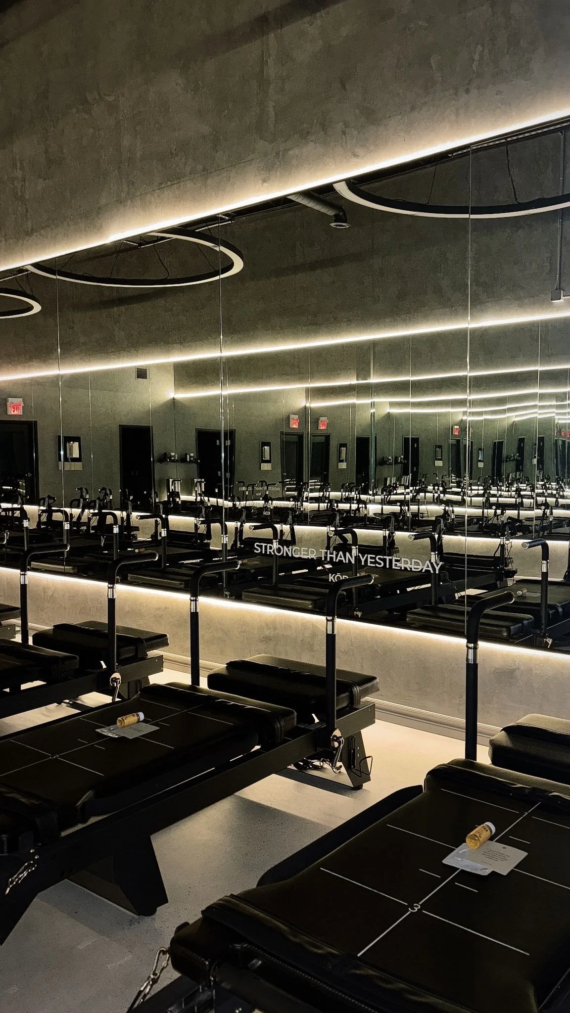 Fitness studio with massage tables, mirrors, and exercise equipment reflected in the mirror, with the phrase 'Stronger Than Yesterday' written on the mirror.