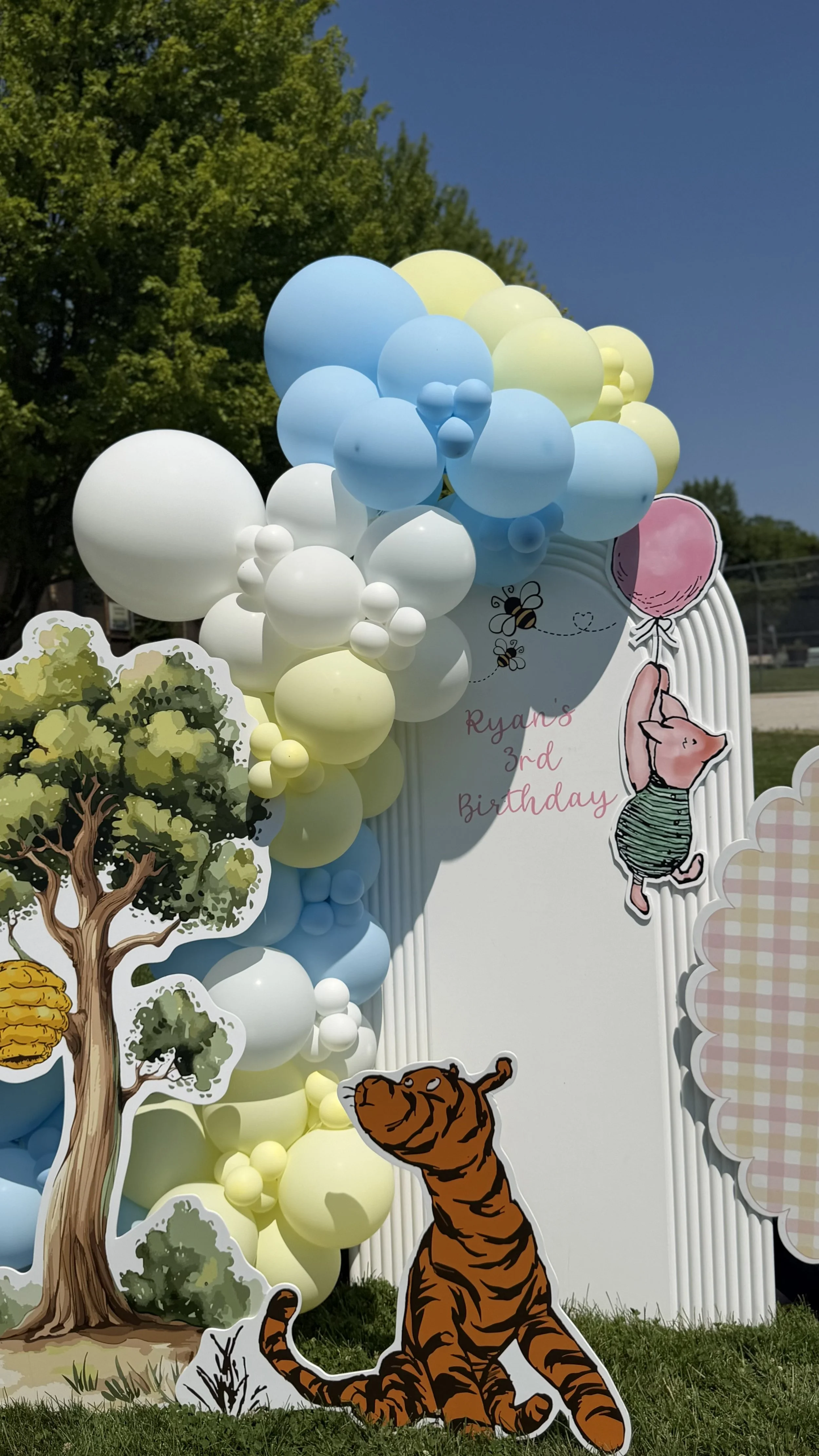 Decorative birthday display with balloons and cutouts of trees, a bear, a tiger, and a cartoon pig, celebrating Ryan's 3rd birthday.