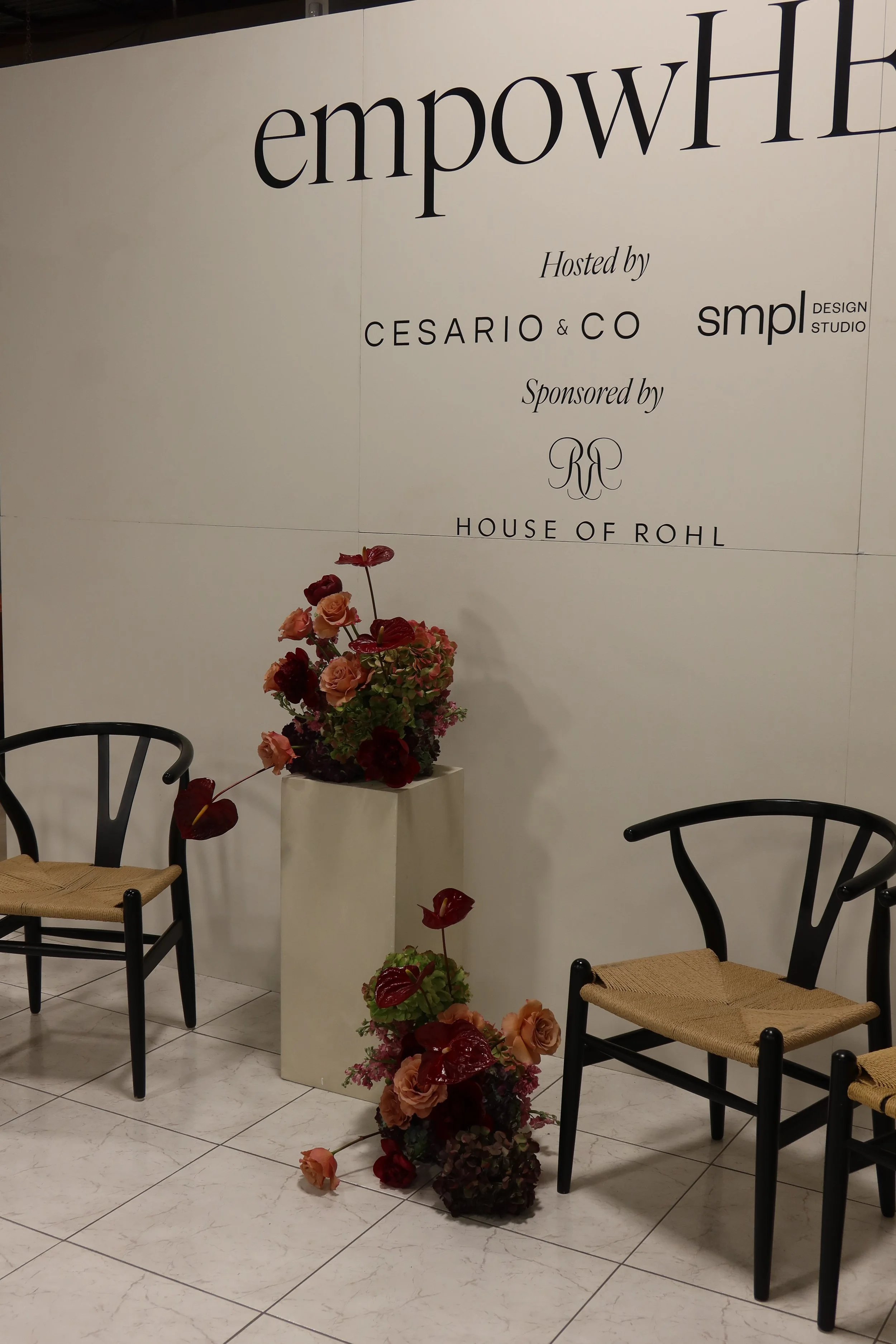 A welcome sign at an event with flowers in a white vase on a table, surrounded by chairs.