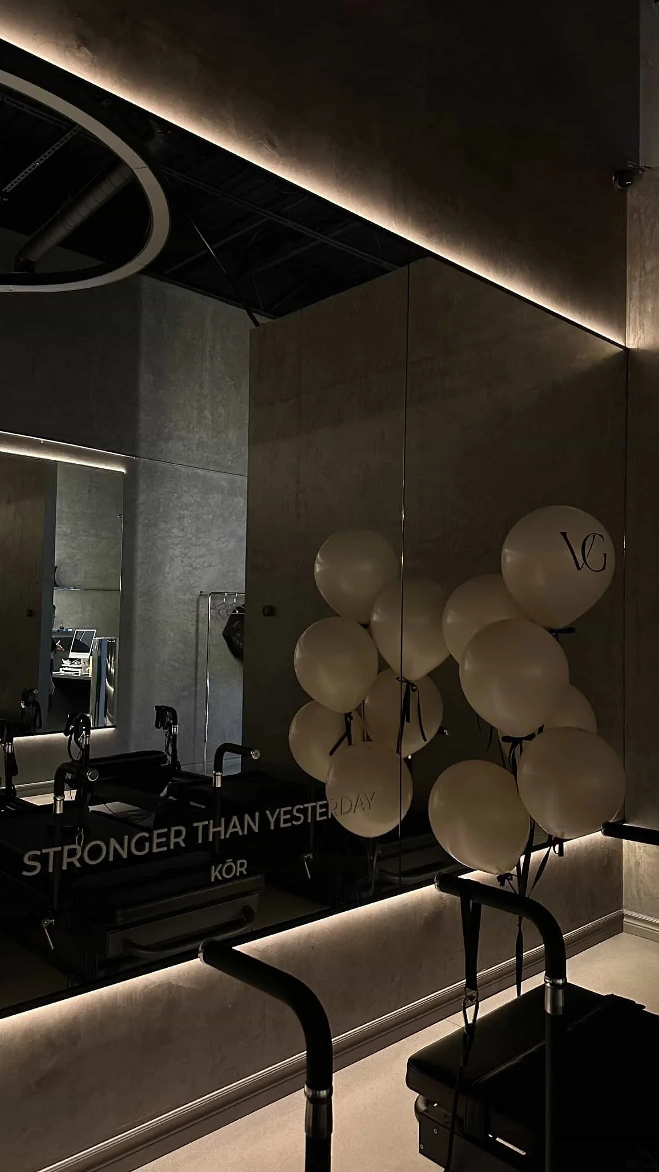 A fitness or Pilates studio with exercise equipment, a row of balloons with ribbons, and a mirror reflecting the room, illuminated by ambient lighting.