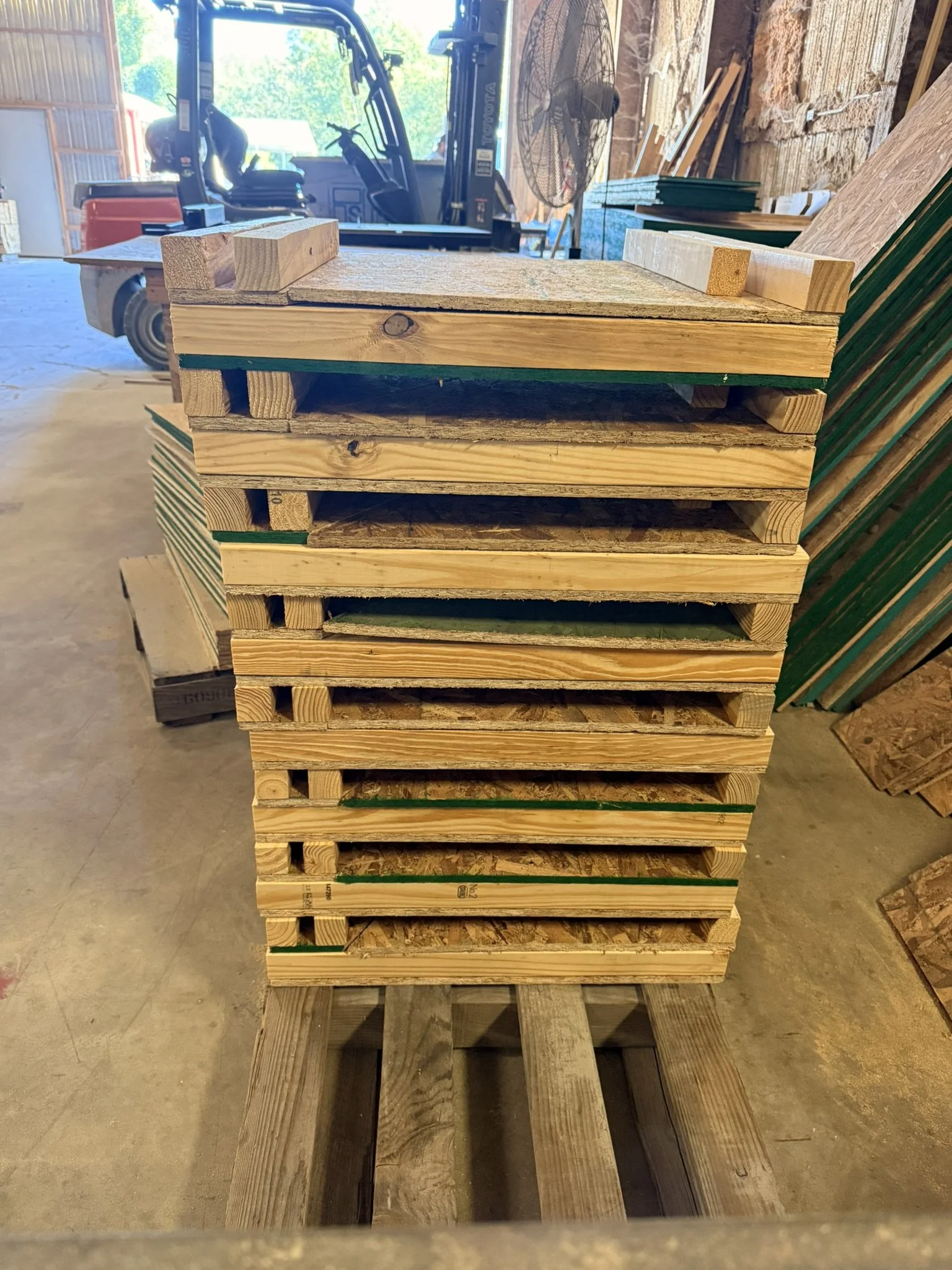 Stacked wooden pallets inside a building, with construction materials and tools visible in the background.