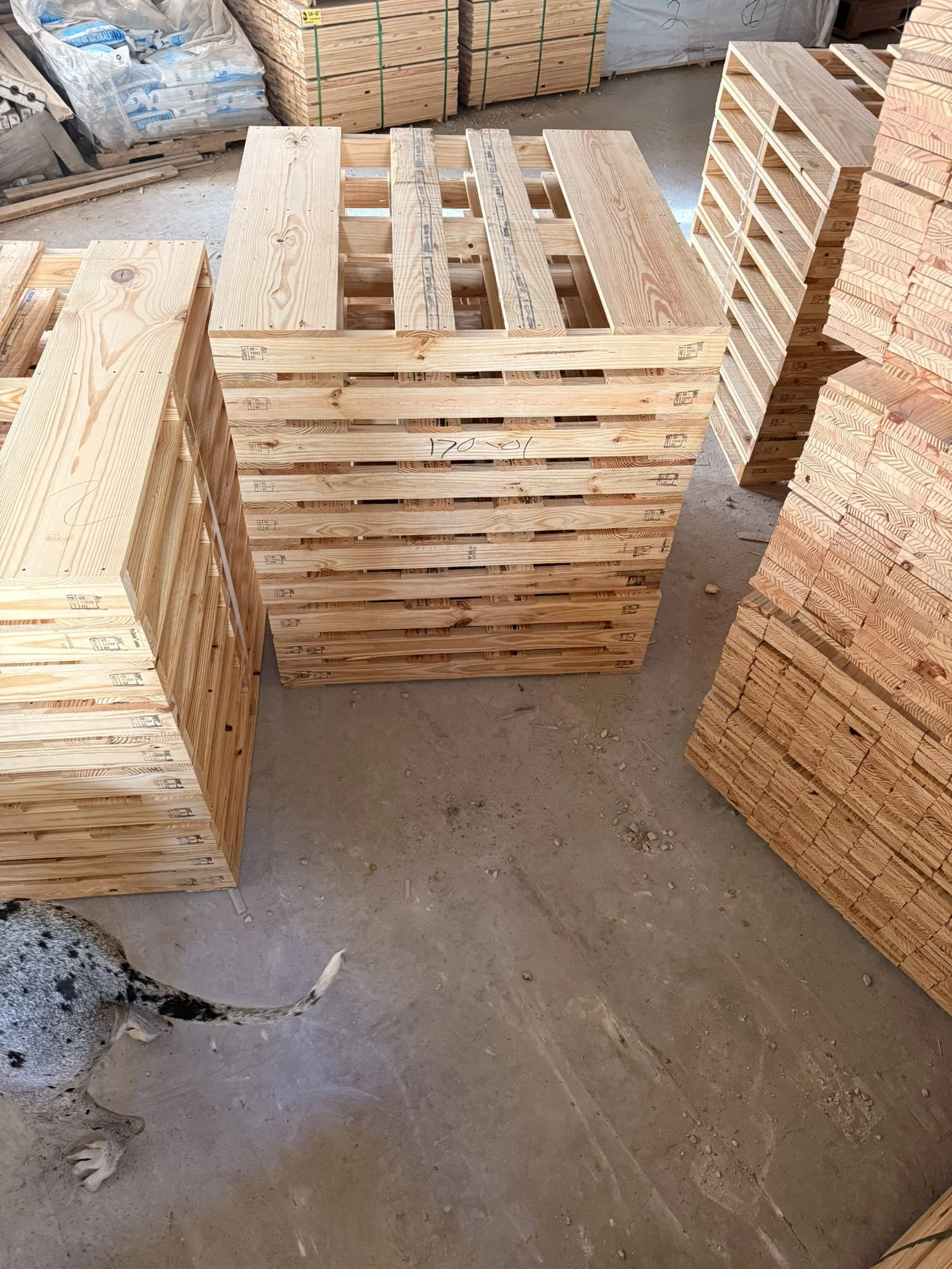 Stack of wooden pallets in a construction or hardware store, with other stacks of wood and building materials in the background.