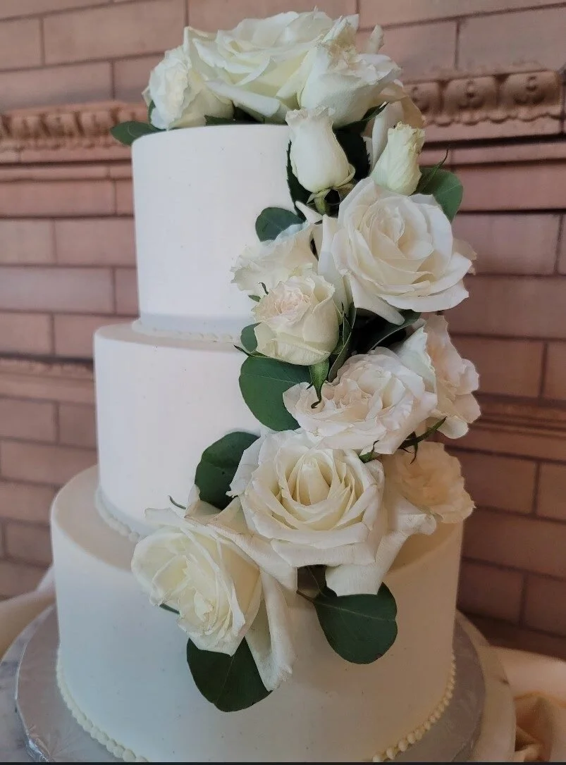 Three-tier white wedding cake decorated with white roses at Union Station Banquets