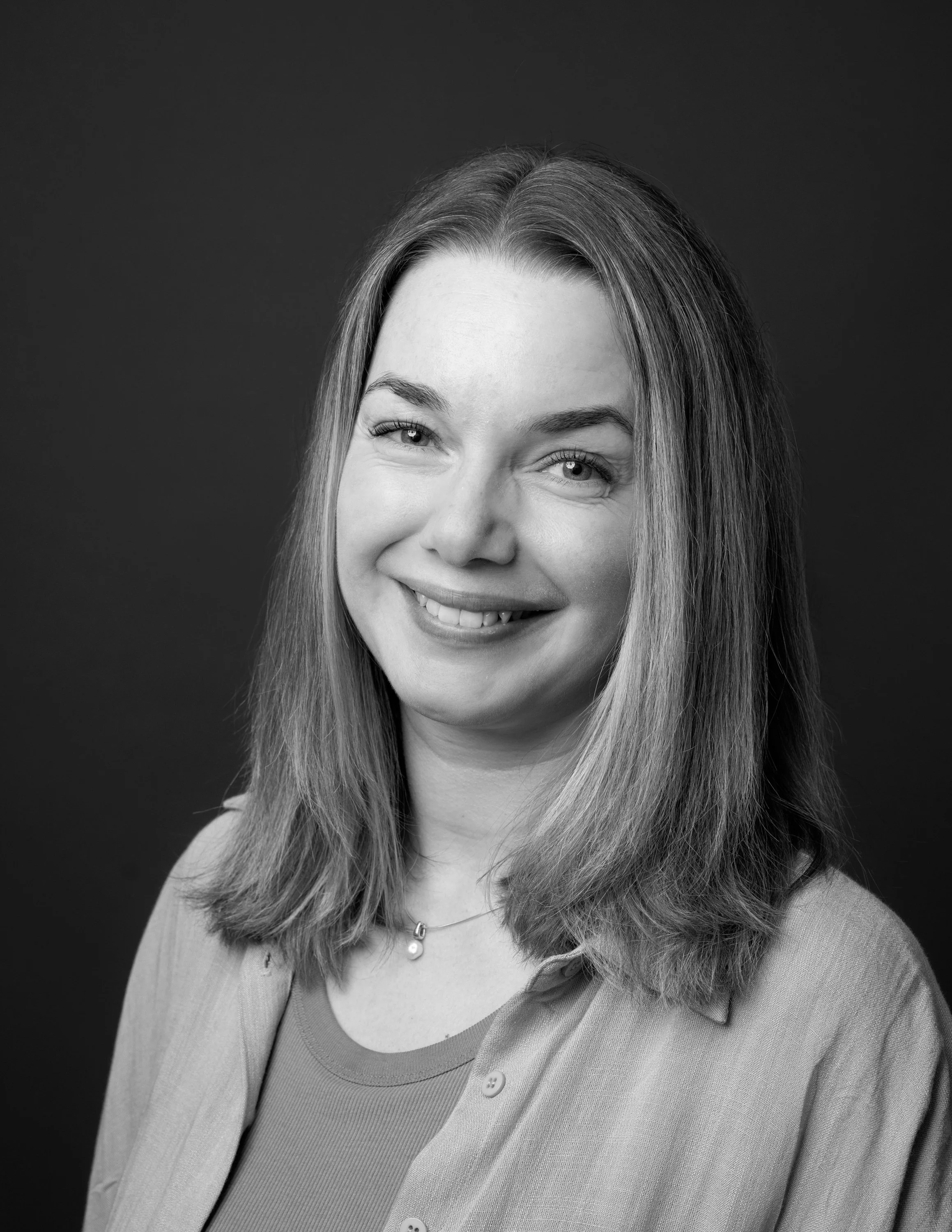 Black and white portrait of a woman smiling with long, straight hair and a light-colored top with a collar and buttons.
