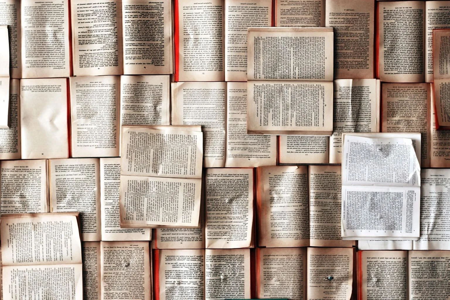 A wall covered in open books arranged in a grid pattern, with some pages overlapping and some partially folded.