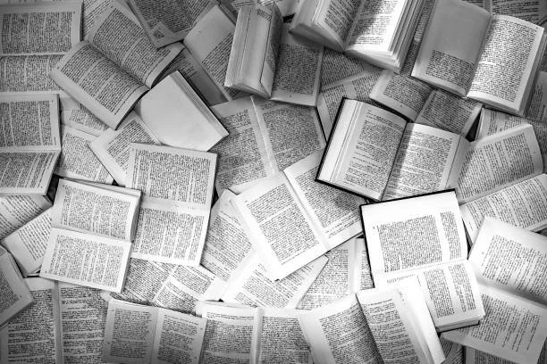 Multiple open books and pages scattered on a surface in black and white