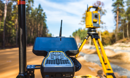 Surveying equipment including a tablet, a GPS antenna, and a total station on a riverbank.