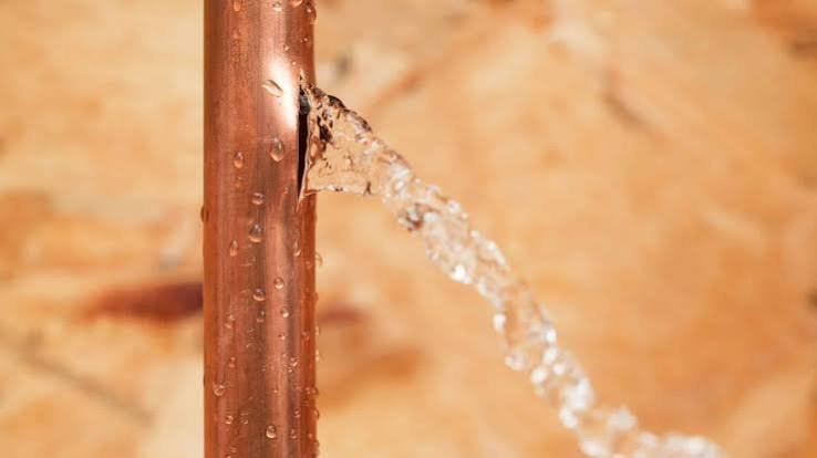 Close-up of a copper pipe with a leak and water dripping from the crack.