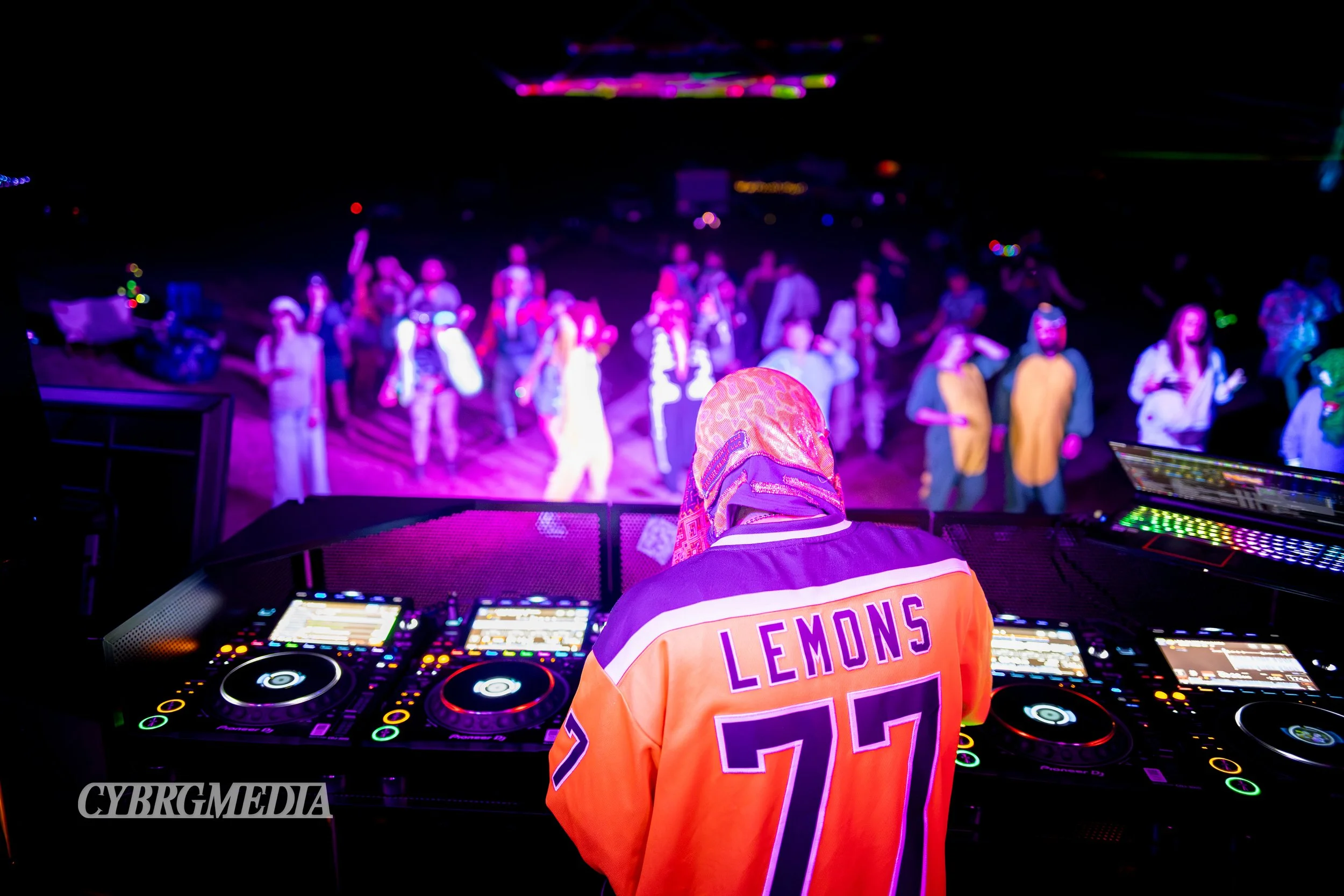 DJ performing at a festival with a crowd dancing, colorful lights.