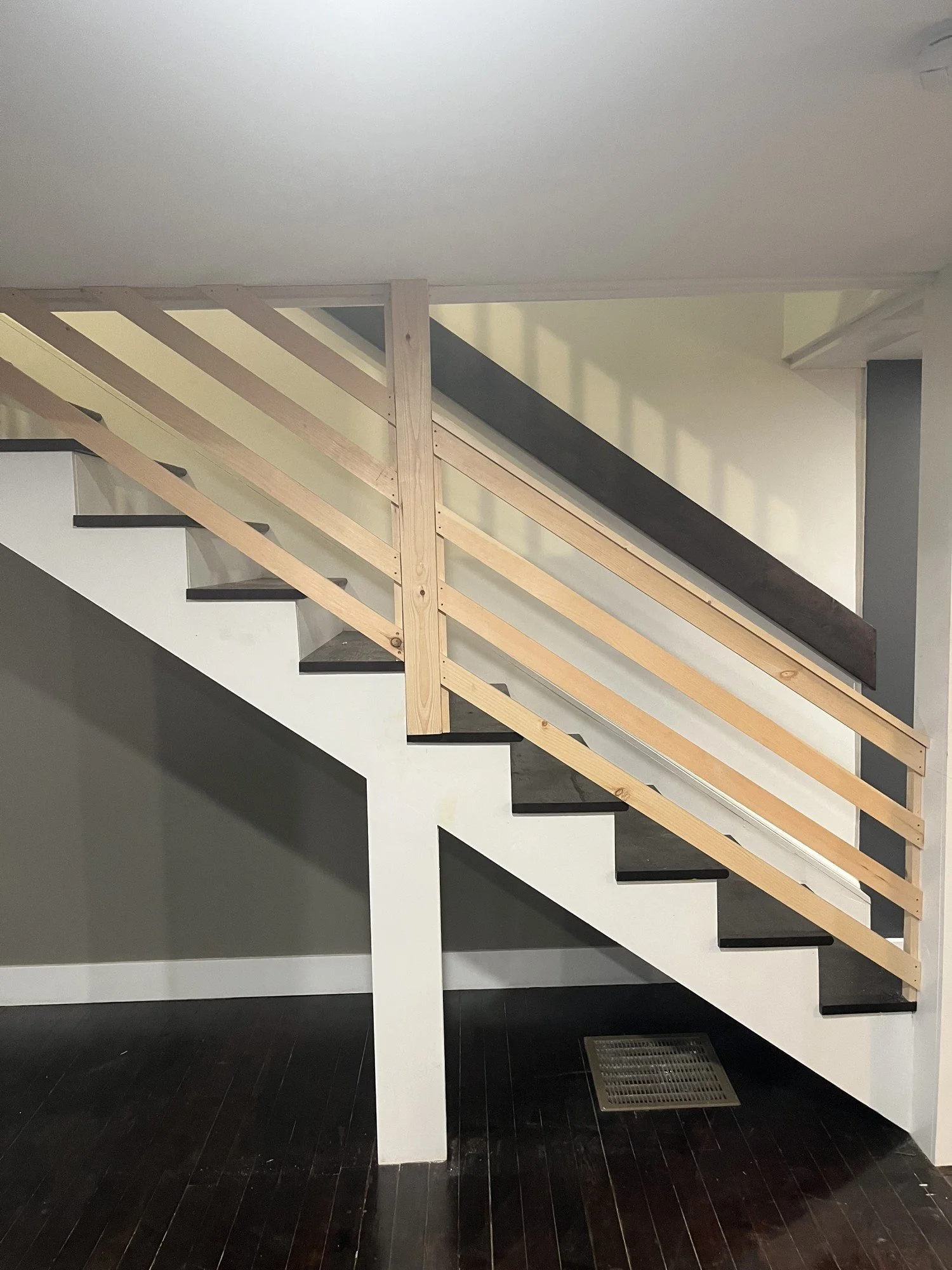 A staircase with black steps and a wooden railing in a modern interior with dark hardwood flooring.