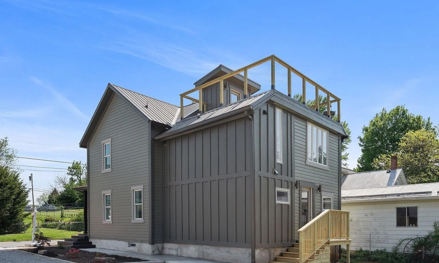 Exterior renovation with new board-and-batten and lap siding, a standing-seam metal roof, new windows and a cable-rail rooftop deck.