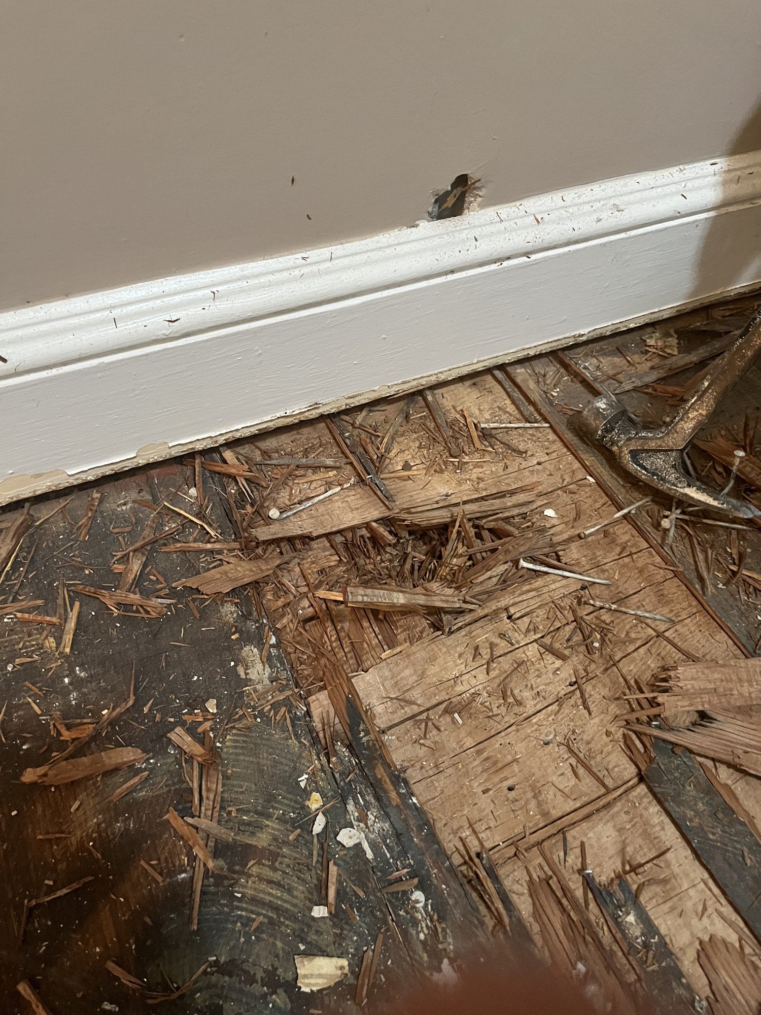 A close-up shot of damaged and burnt wooden subfloor with scattered debris and small wood splinters, showing signs of fire or water damage.