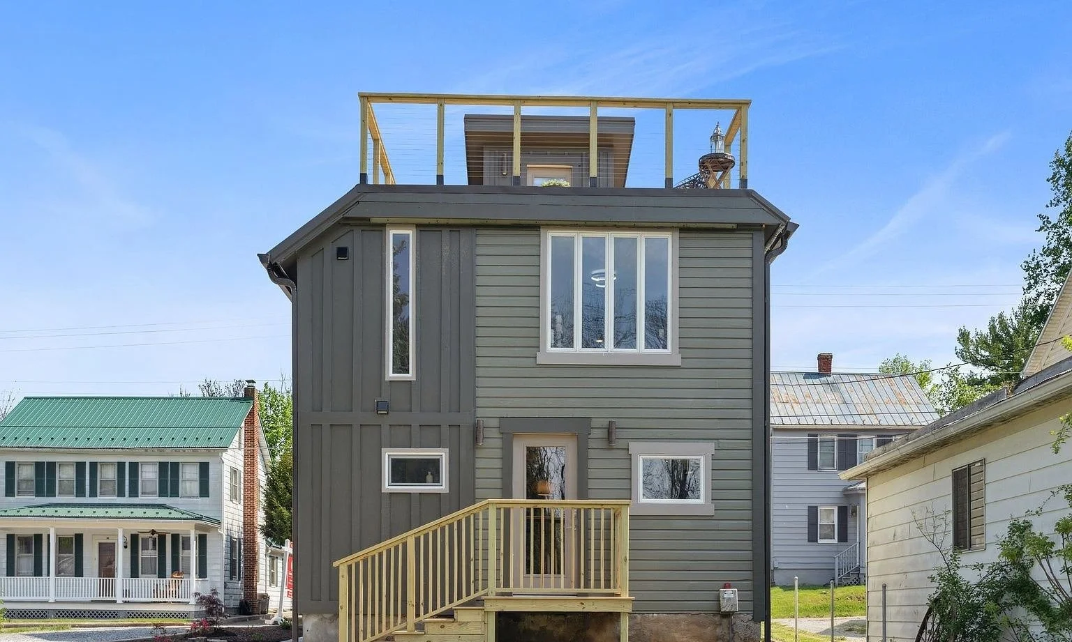 Rear view of a full exterior renovation, with new board-and-batten and lap siding, new windows, a rooftop deck and new entry stairs.