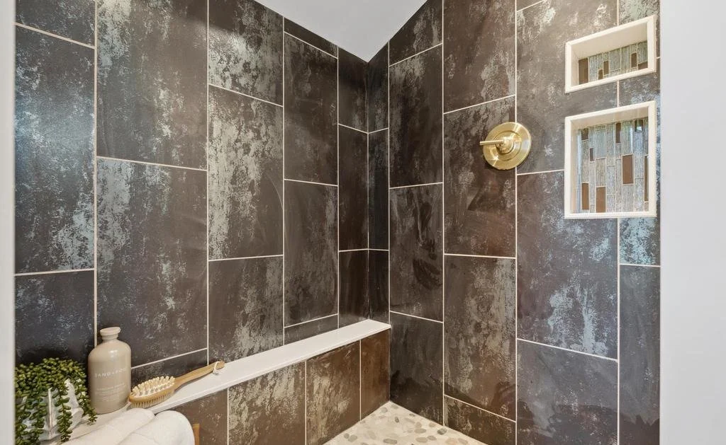 Walk-in tile shower with a built-in bench, lit niches and brass fixtures.