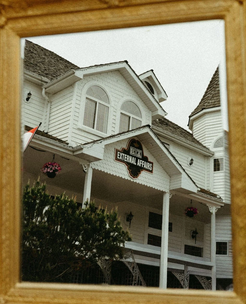 In gold antique ornate frame, the front of iconic External Affairs Medical Spa Victorian-style building in St. Albert Alberta with the building painted white and restored beautifully