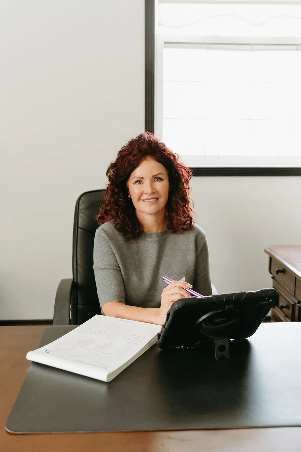 Dr. Marcia Hartt sitting in a chair behind a desk at External Affairs Medical Spa performing a facial balancing consultation with patient