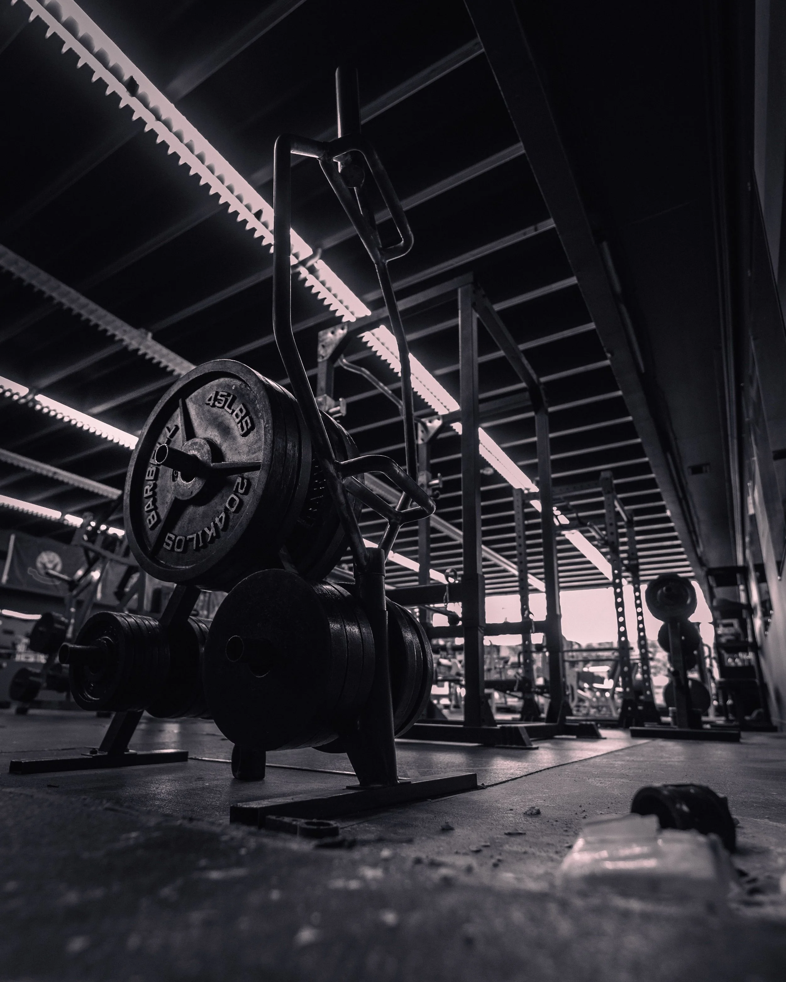 A gym with a barbell loaded with weights on a squat rack, illuminated by overhead lighting, with a focus on the iron weights and the gym floor.
