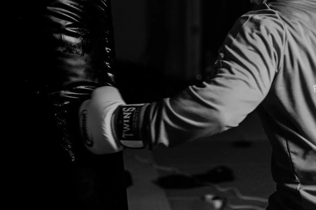 A person wearing a sports glove is practicing boxing, hitting a punching bag in a gym.