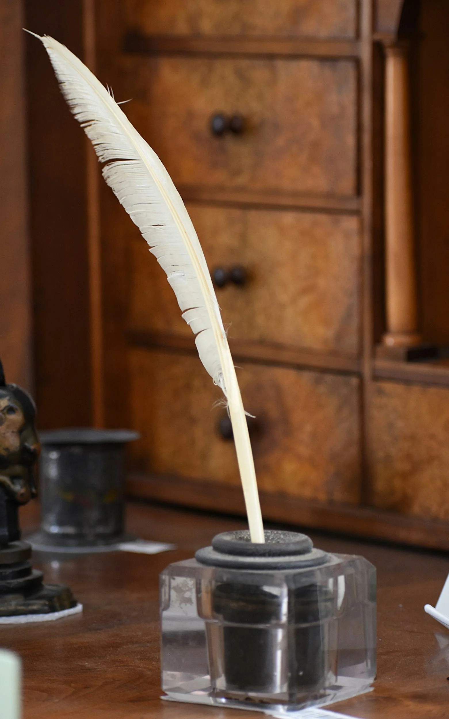 White feather in an inkwell on a desk.