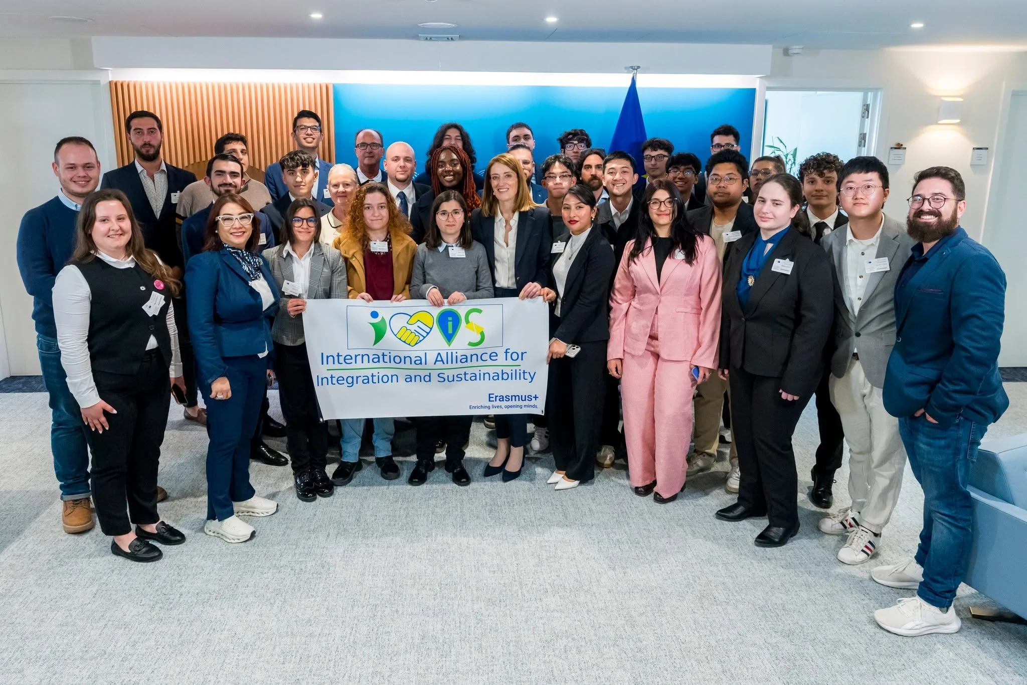 A diverse group of people posing together indoors for a photo at a conference or event, holding a banner that reads 'International Alliance for Integration and Sustainability'.