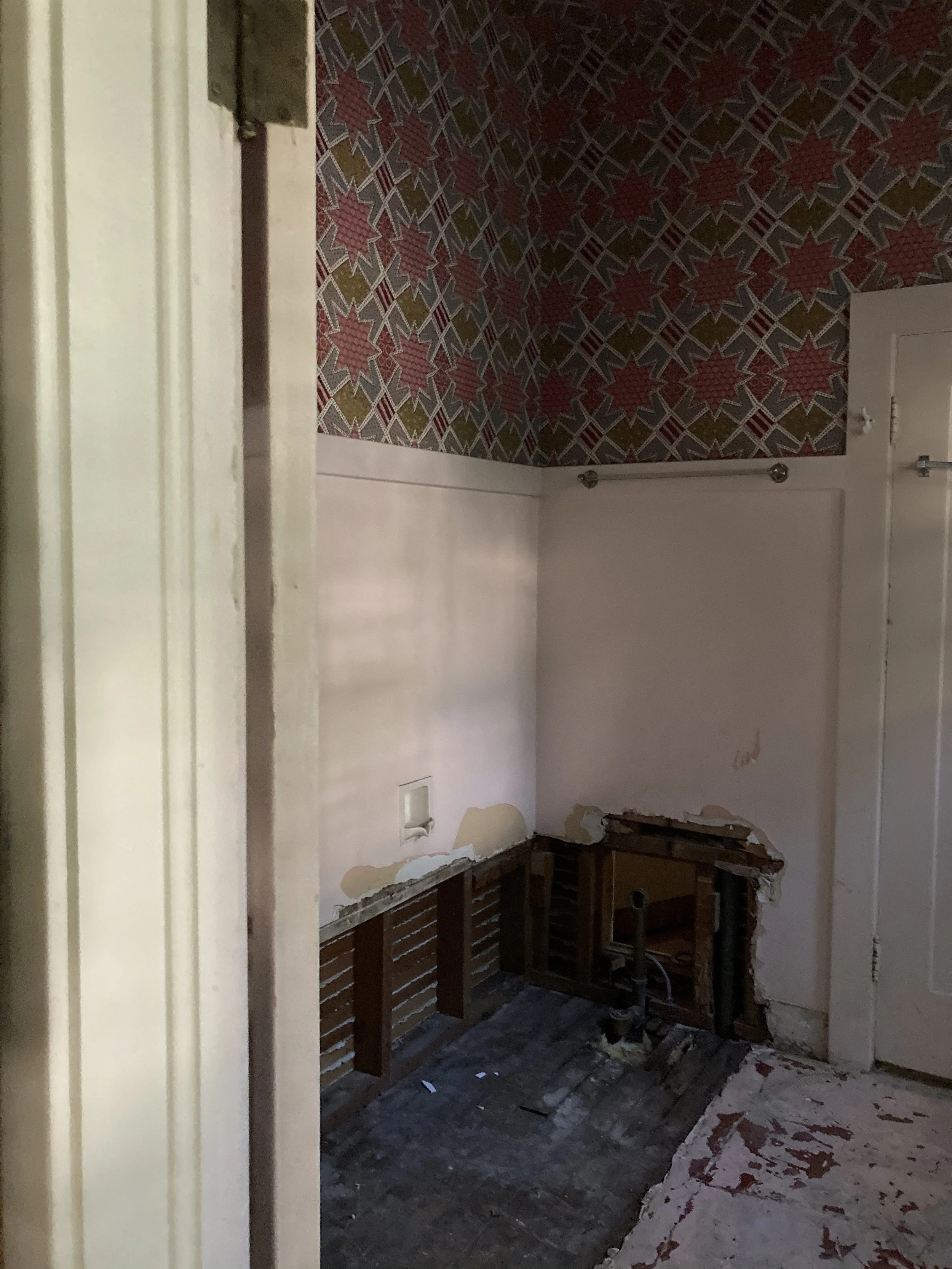 A room under renovation with exposed plumbing, damaged wall with peeling paint, and construction debris on the floor.