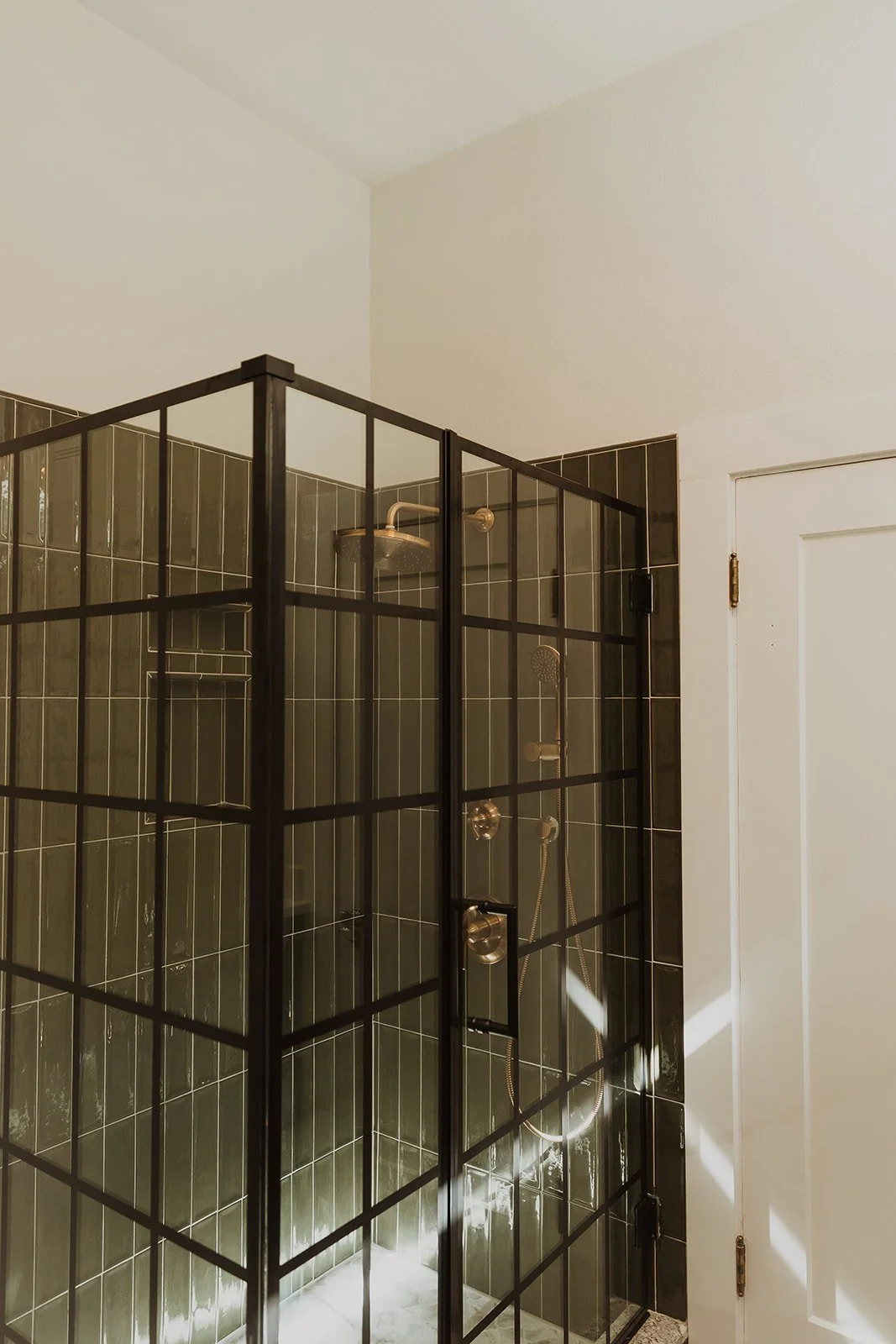 A modern shower enclosure with black metal grid design and dark green tiles inside.