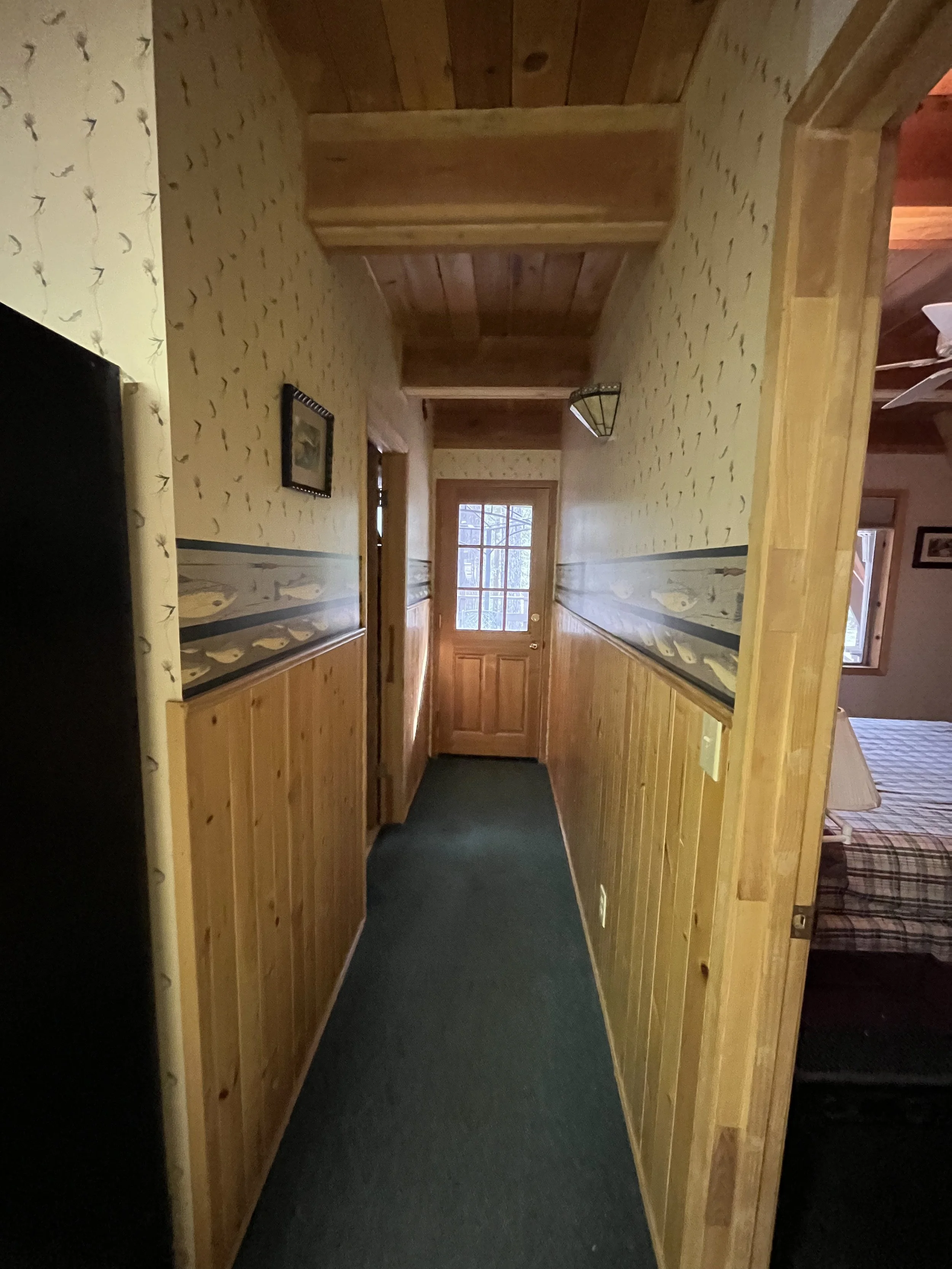 Wood-paneled hallway with artificial lighting, leading to a door with a window, and a framed picture on the wall.