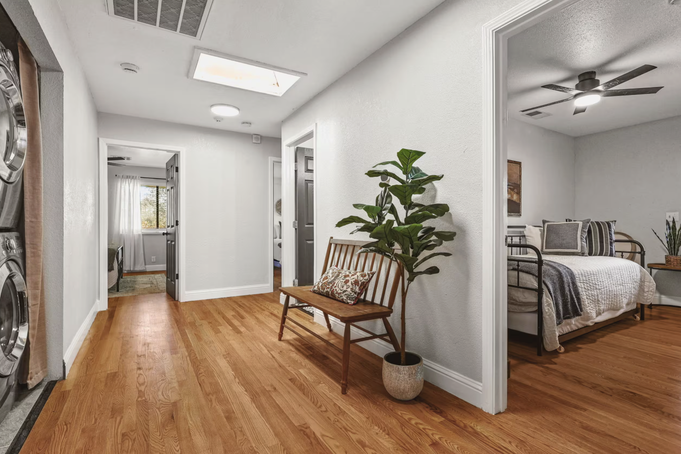 Interior view of a hallway and bedroom with hardwood floors, white walls, and ceiling fan.
