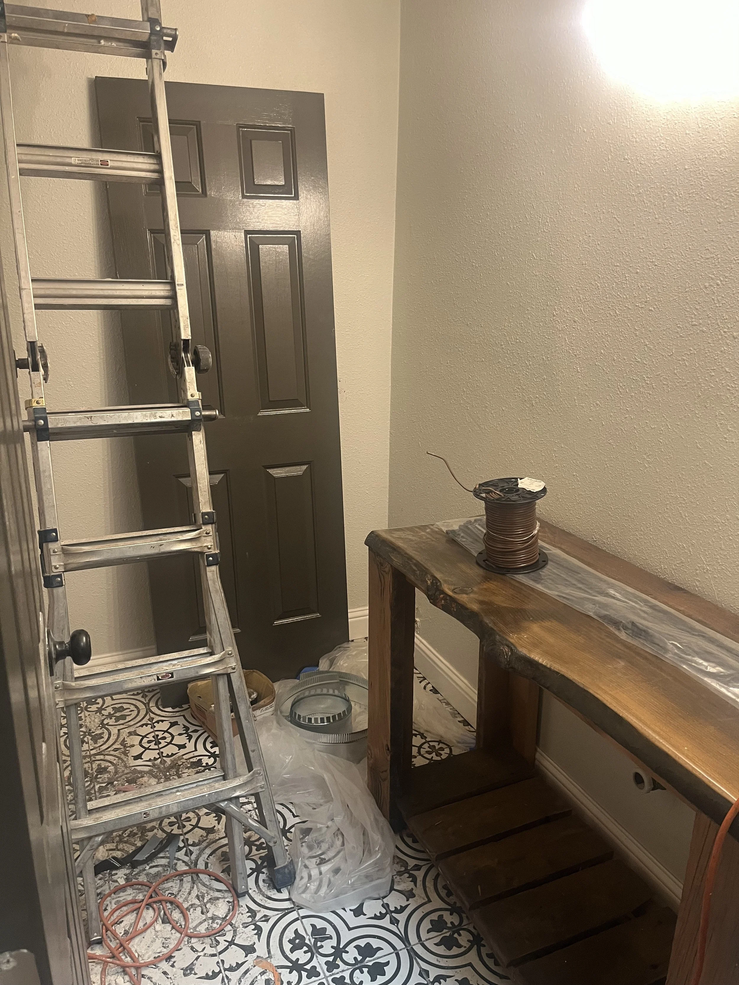 Construction or renovation room with a metal stepladder, a black door, a wooden table, and various tools and supplies.