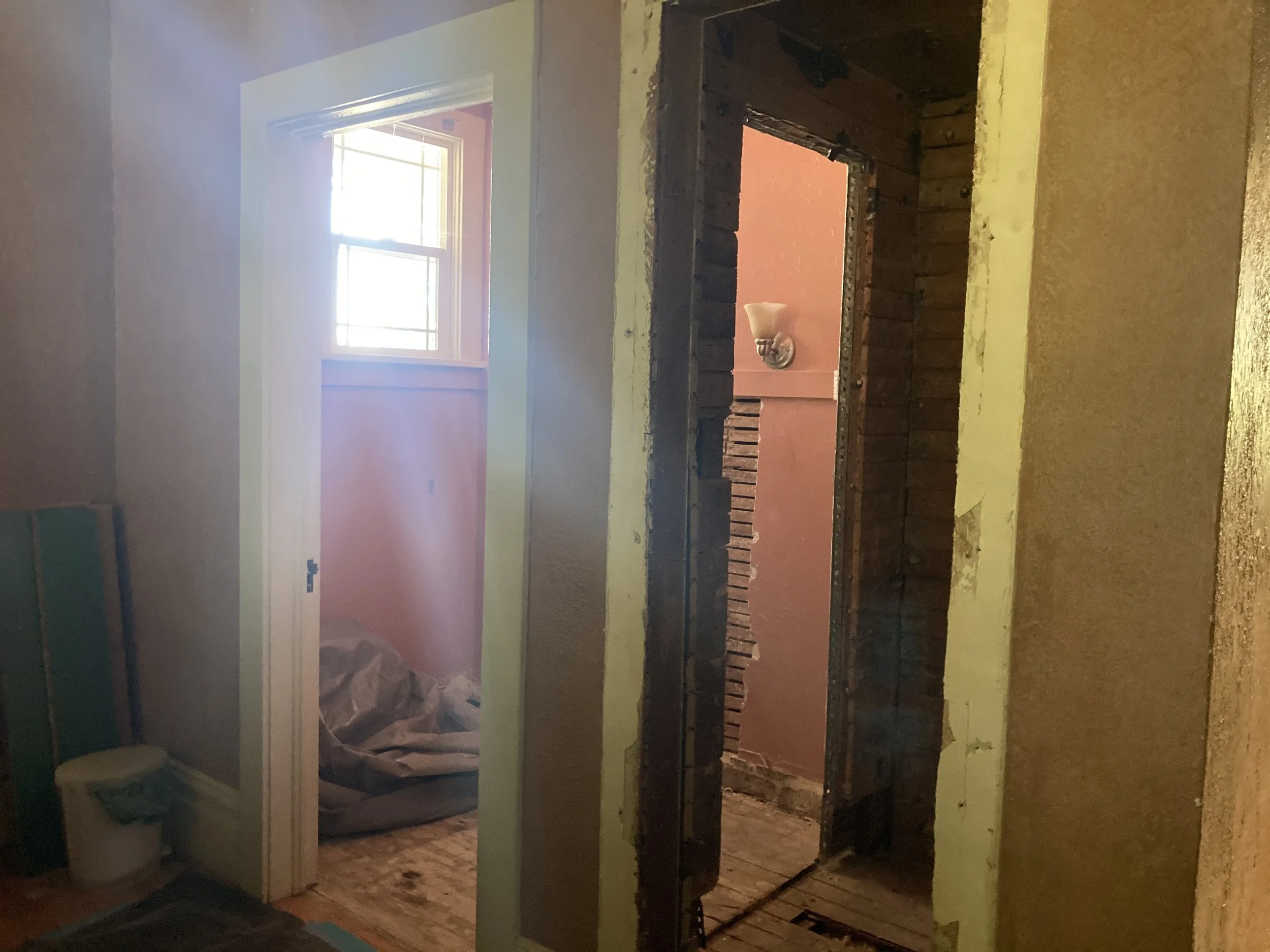 Interior view of a room under renovation with exposed brick walls and a window, showing insulation and construction materials.