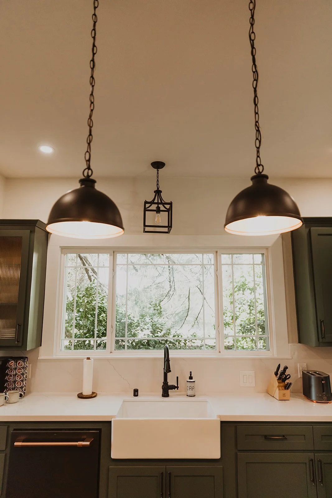 Kitchen with black pendant lights, a farmhouse sink, and a view of trees outside the window.
