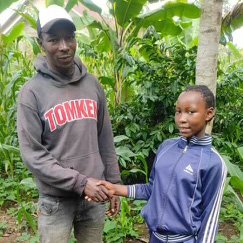 Two males shaking hands outdoors in a lush green tropical setting.