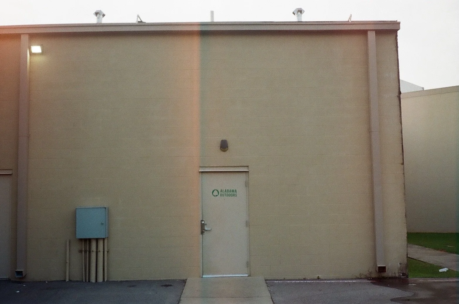 Back of a beige building with a white door labeled "Alabama Outdoors."