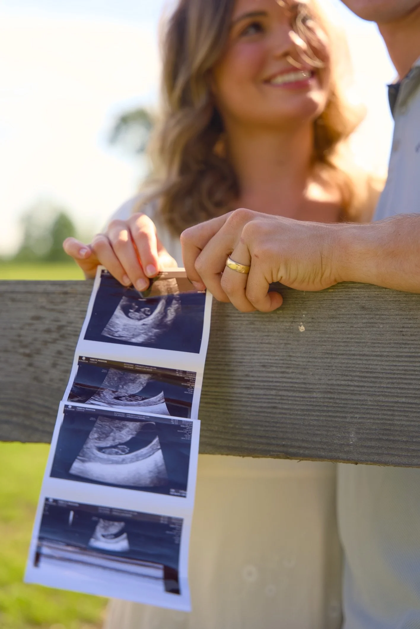 A woman is looking at an ultrasound photo that is hanging on a wooden fence in an outdoor park or garden setting.