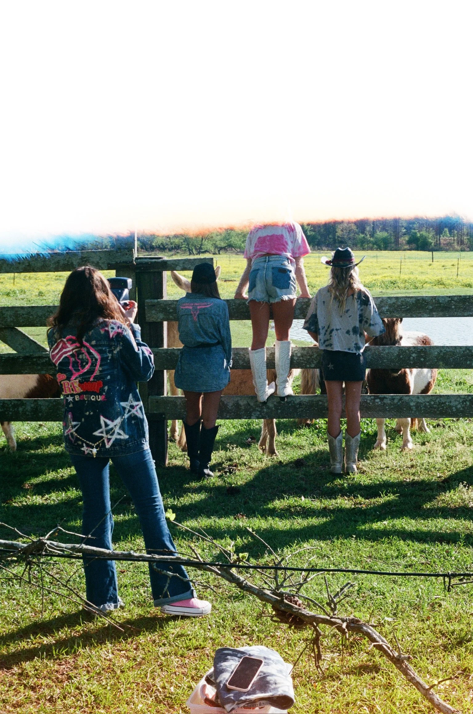 Four people and a dog at a farm, watching cows by a pond with a wooden fence, sunny day, trees in the background.