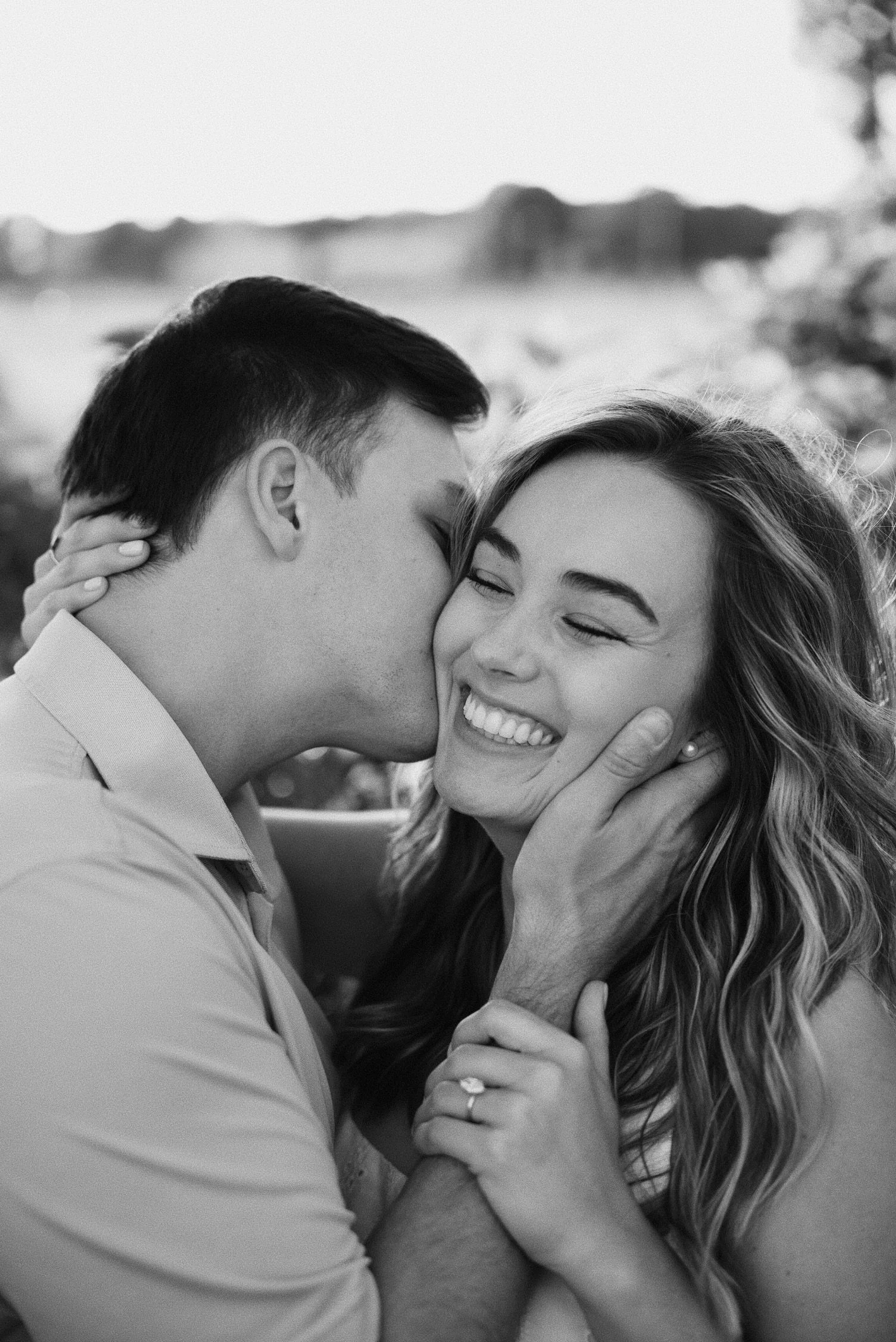 A black and white photo of a man and woman sharing a kiss, with the woman smiling and the man holding her face gently.