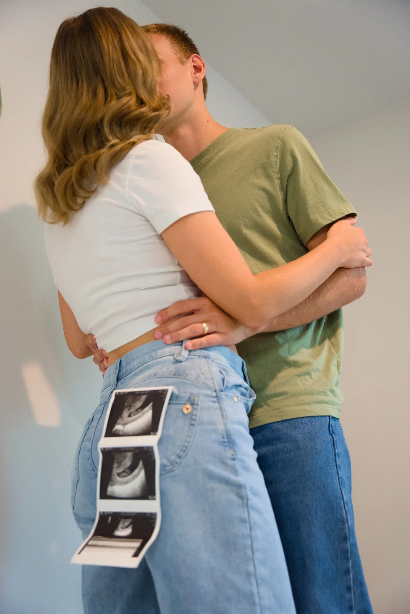 A couple sharing a kiss, with ultrasound pictures attached to the woman's jeans, suggesting pregnancy.