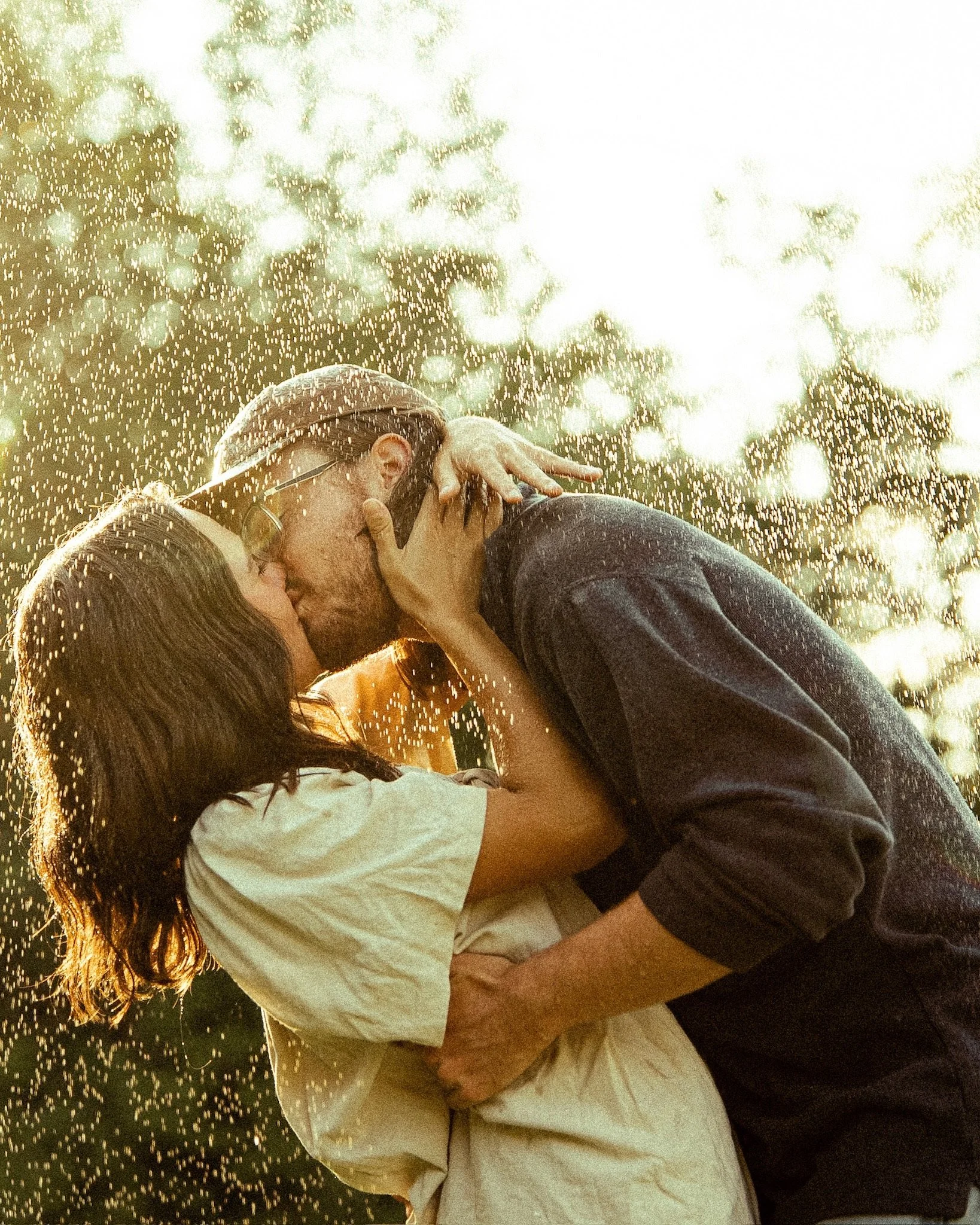A couple sharing a kiss in rain, with sunlight reflecting off the water droplets.