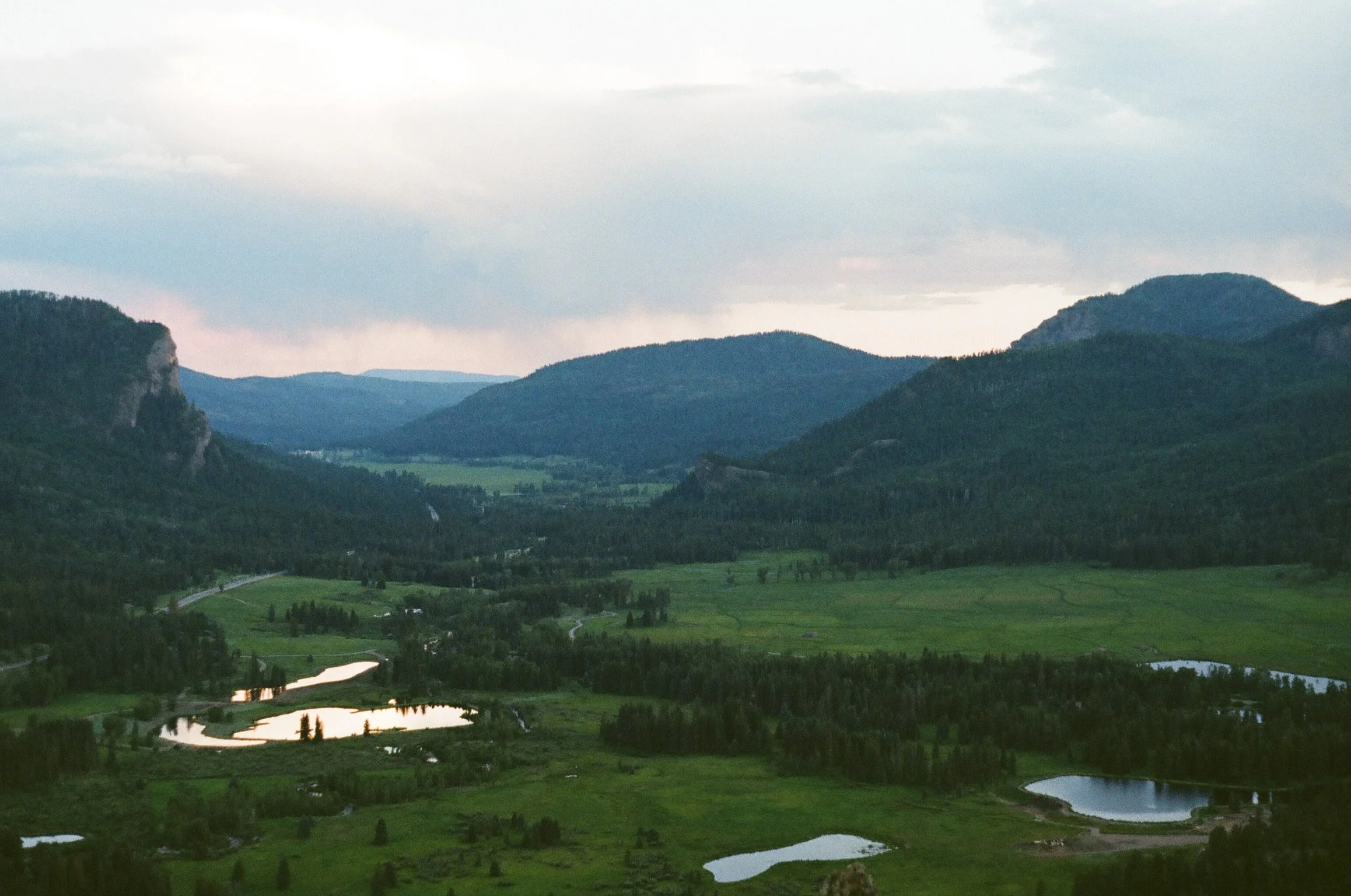 Scenic landscape of green rolling hills, winding rivers, and distant mountains under cloudy sky.