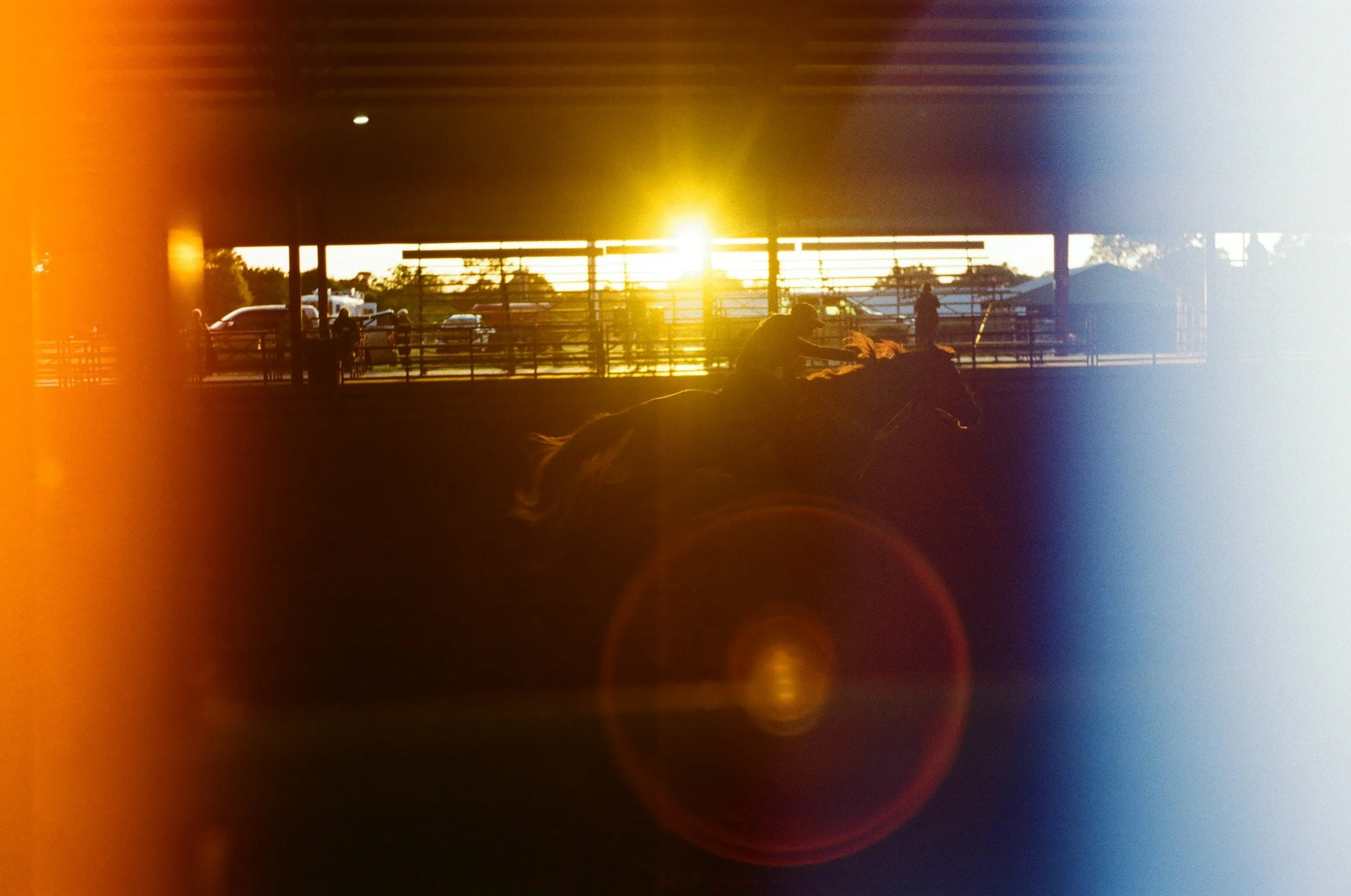 Sunset over a parking lot with silhouetted people and cars, with a warm glow and lens flare effects.