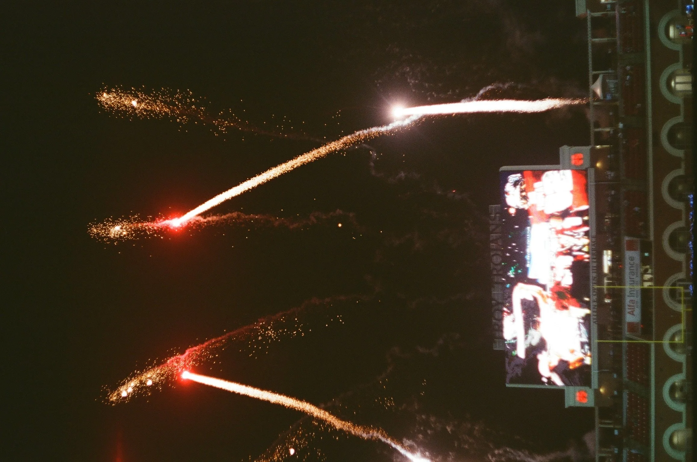 Nighttime scene at a sports stadium with fireworks and a digital scoreboard visible.