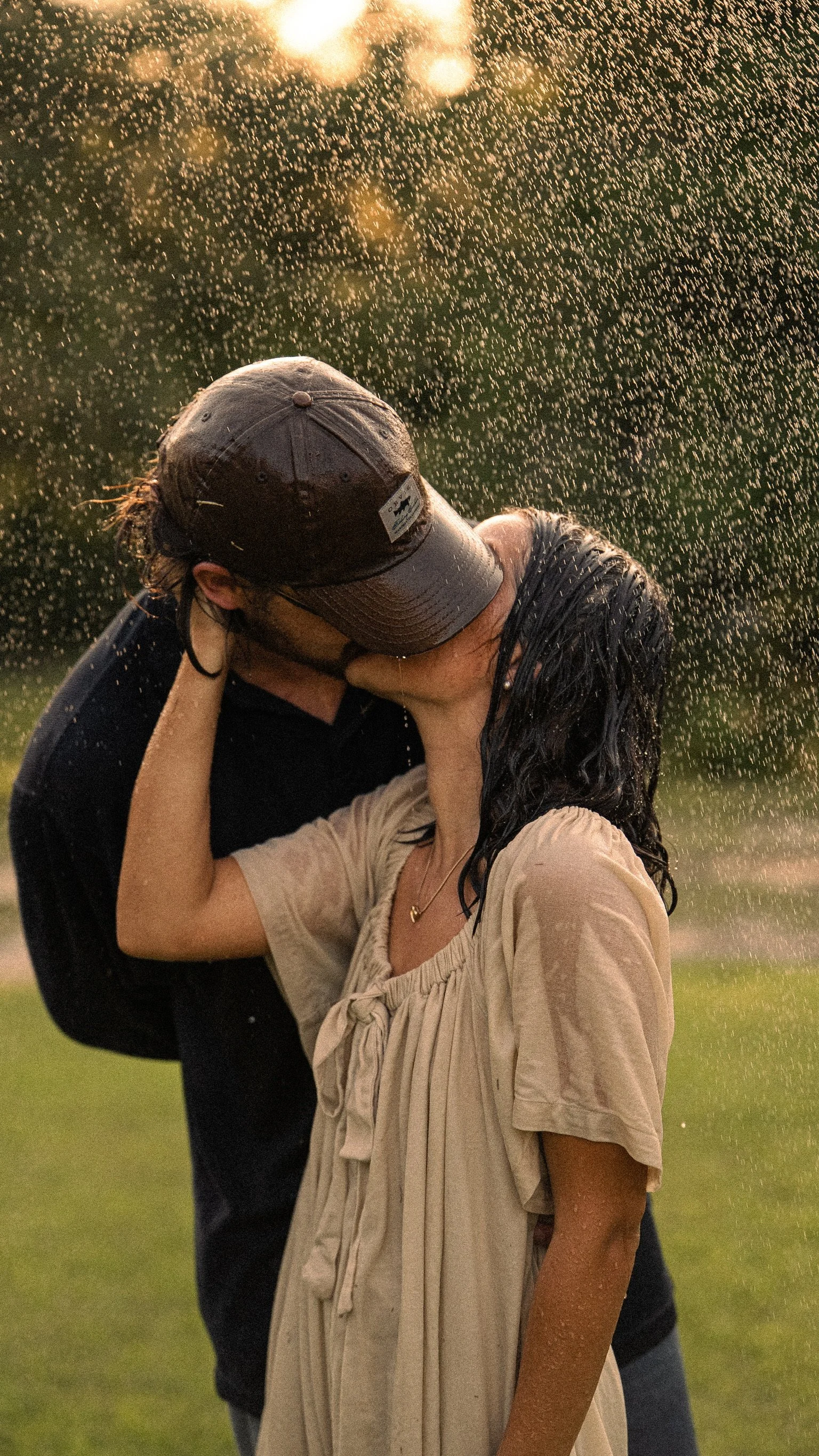 A couple kissing outdoors at sunset with water droplets falling around them.